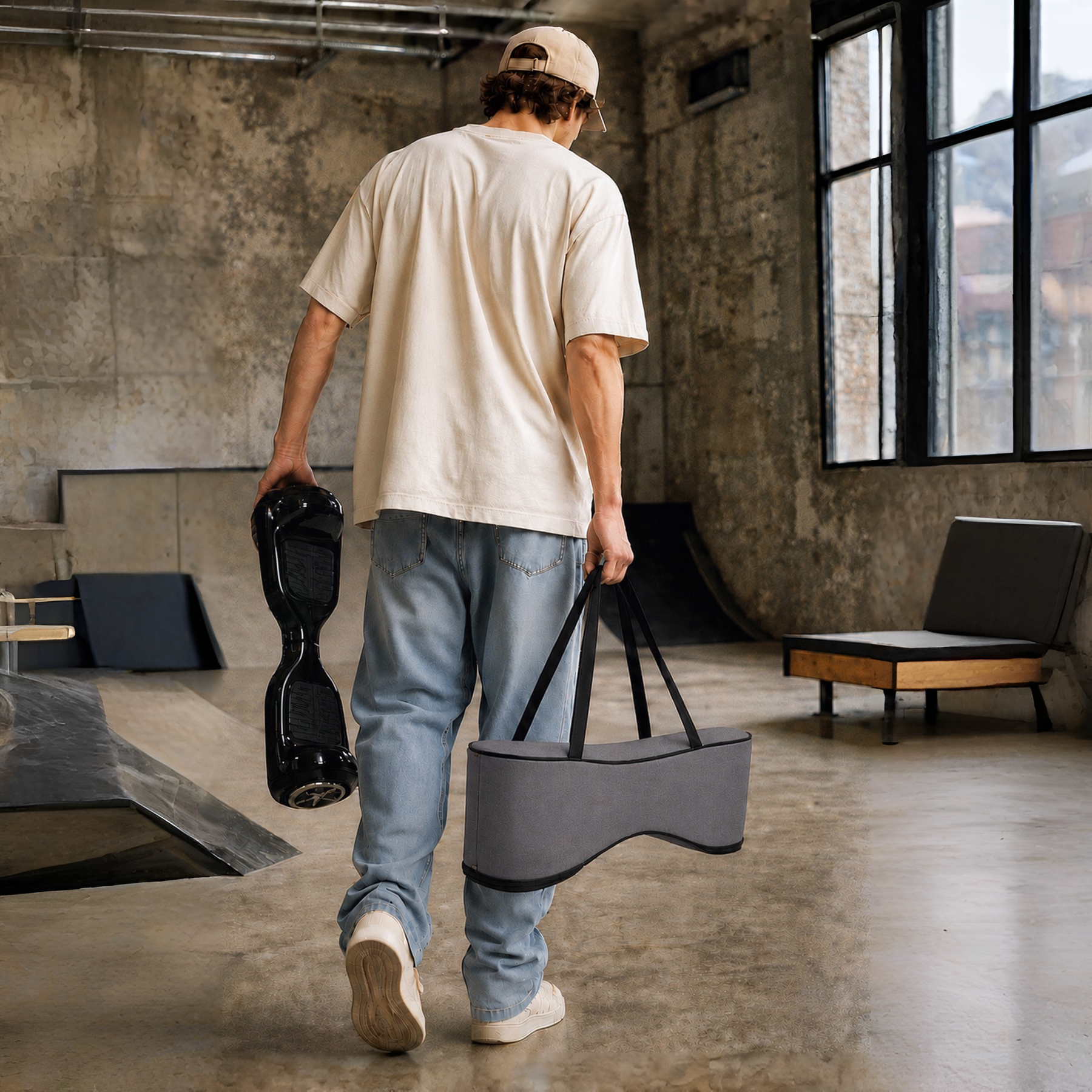 Siyah bir hoverboard ve gri bir çanta taşıyan bir adam kaykay parkında yürüyor.