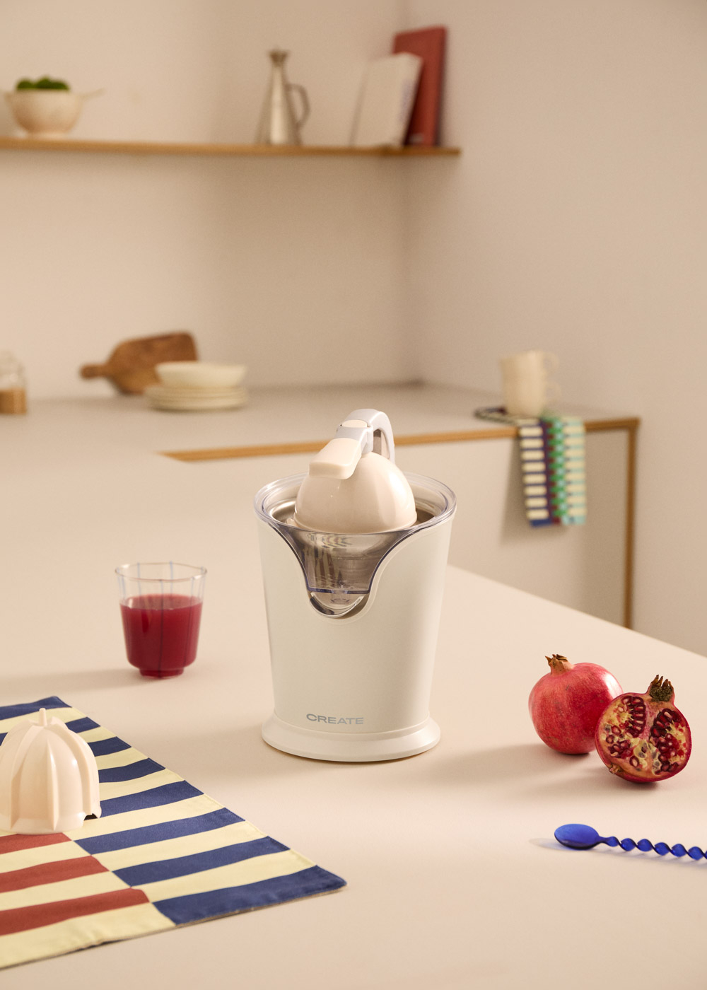 Un exprimidor blanco en una encimera de cocina con granadas, jugo y decoraciones al fondo.