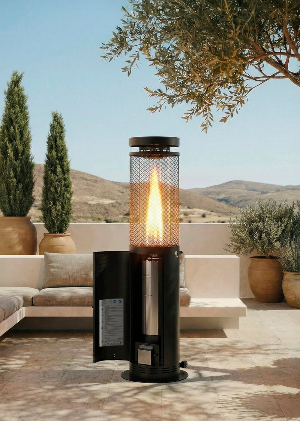 Un calefactor de patio negro con una llama encendida se encuentra en una terraza soleada rodeada de árboles.