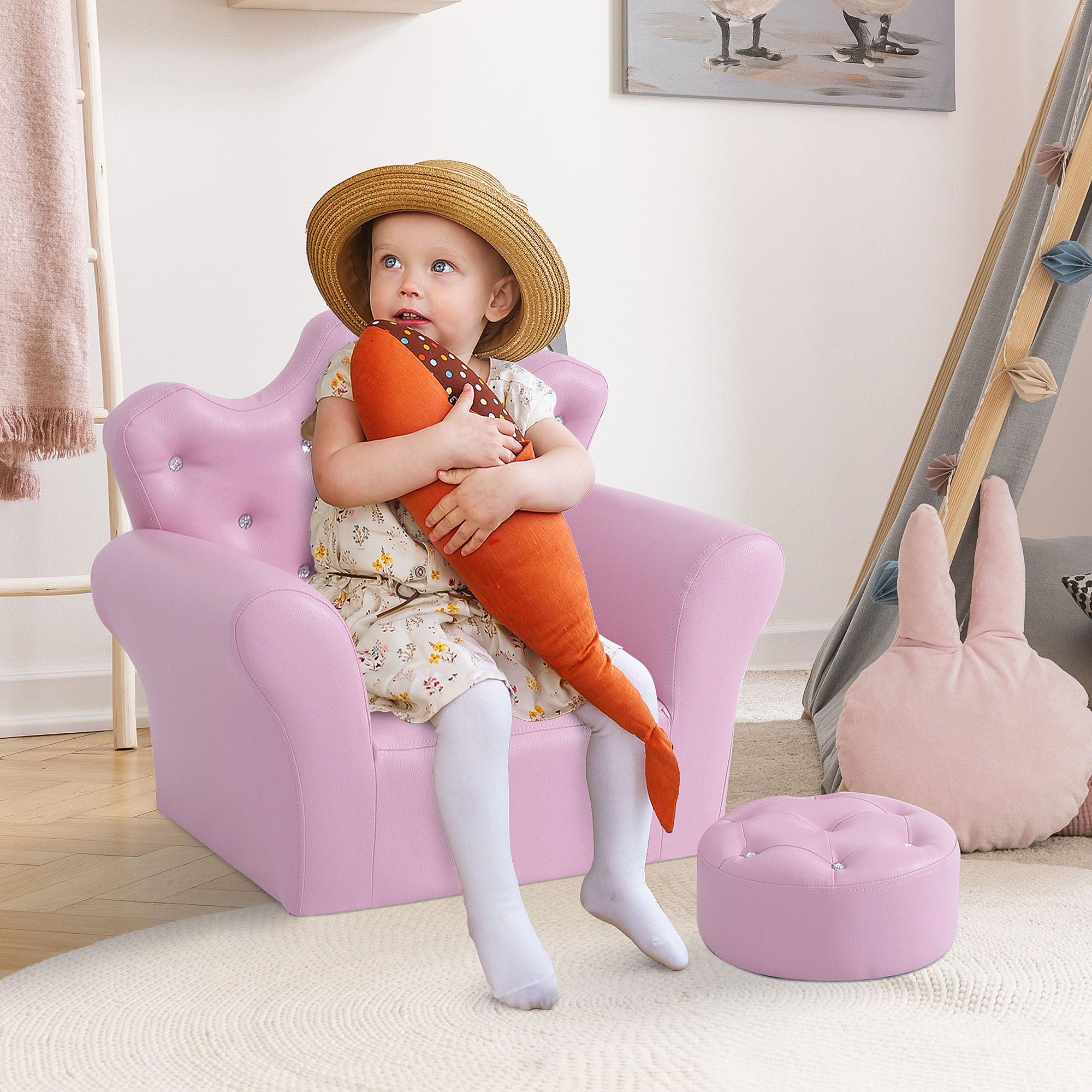 Un niño pequeño con sombrero de paja y vestido floral se sienta en un sillón rosa, sosteniendo una zanahoria.