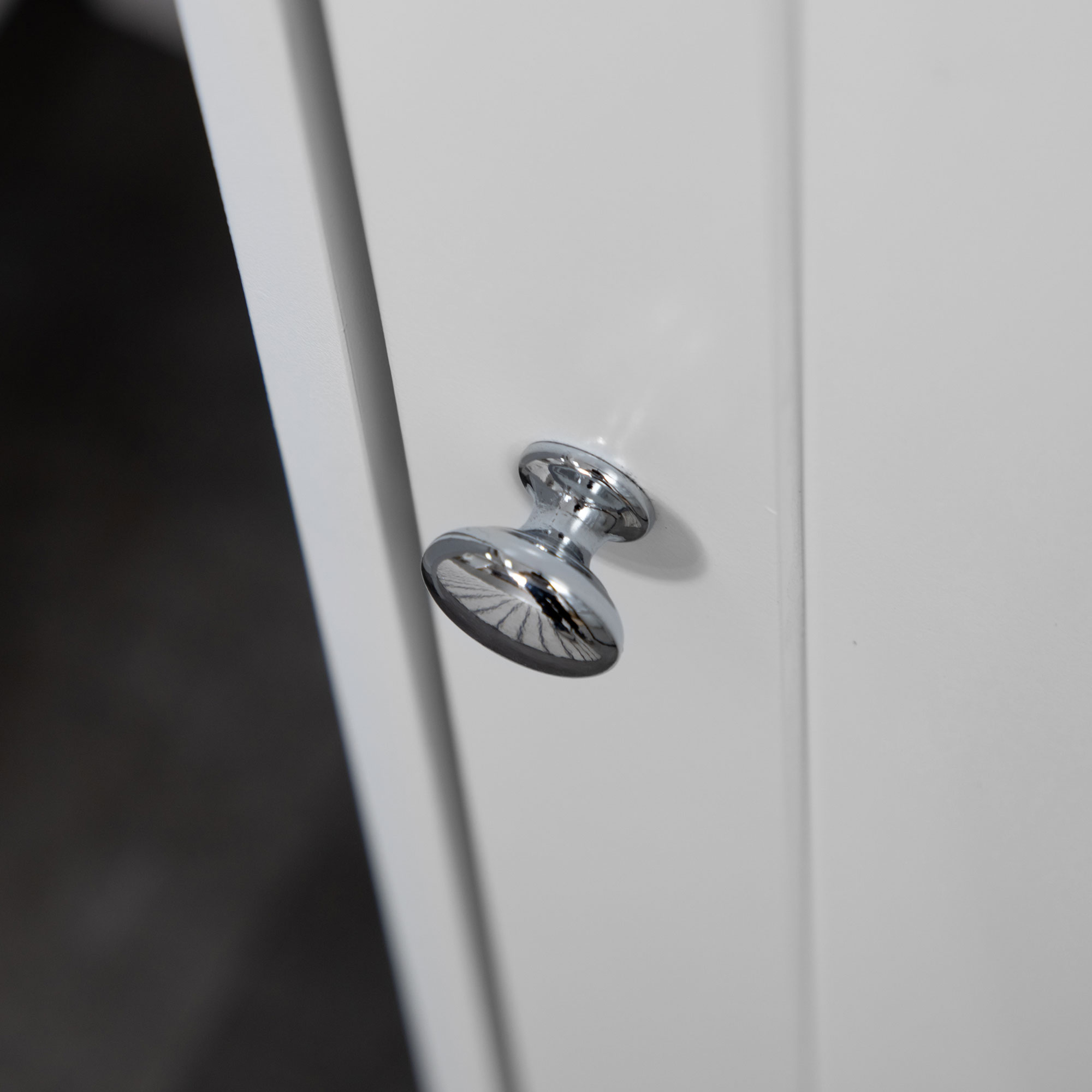 Un tirador de puerta plateado y brillante en una puerta de armario blanca.