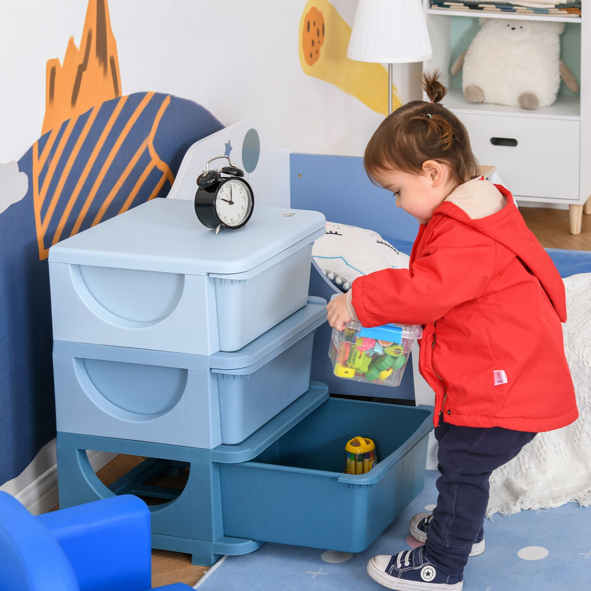 Un niño con chaqueta roja organiza juguetes en cajas de plástico azules dentro de una habitación colorida.