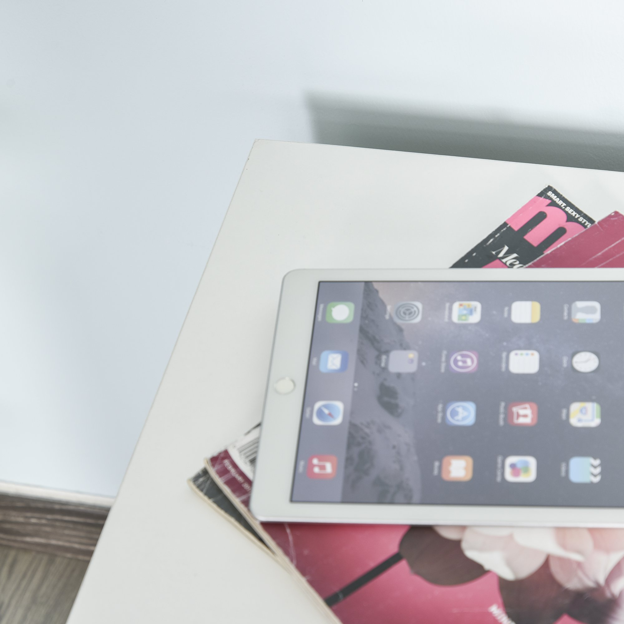 Una tableta plateada con aplicaciones descansa sobre una revista en una mesa blanca.