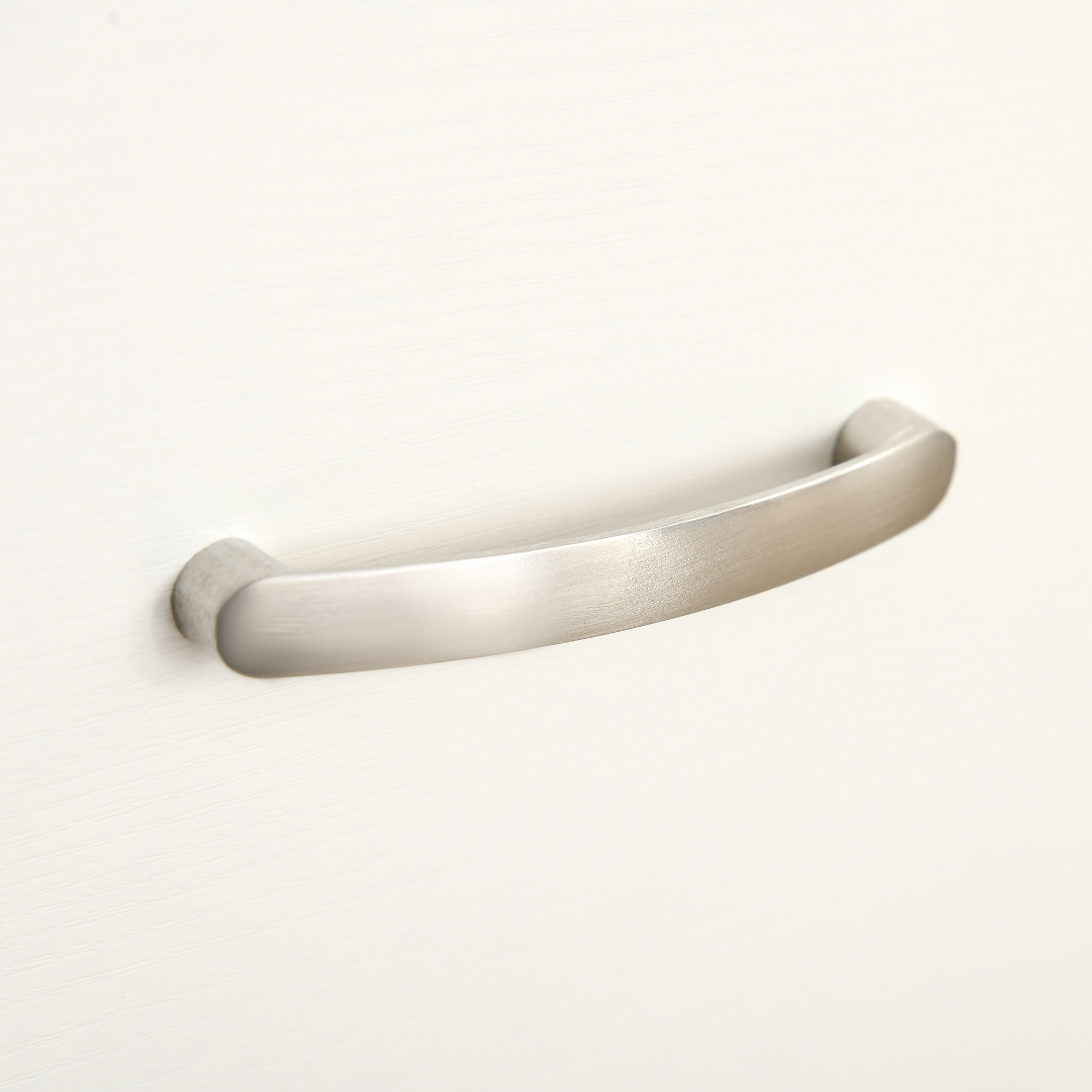 Un tirador de mueble de metal plateado montado en un frente de cajón blanco texturizado.