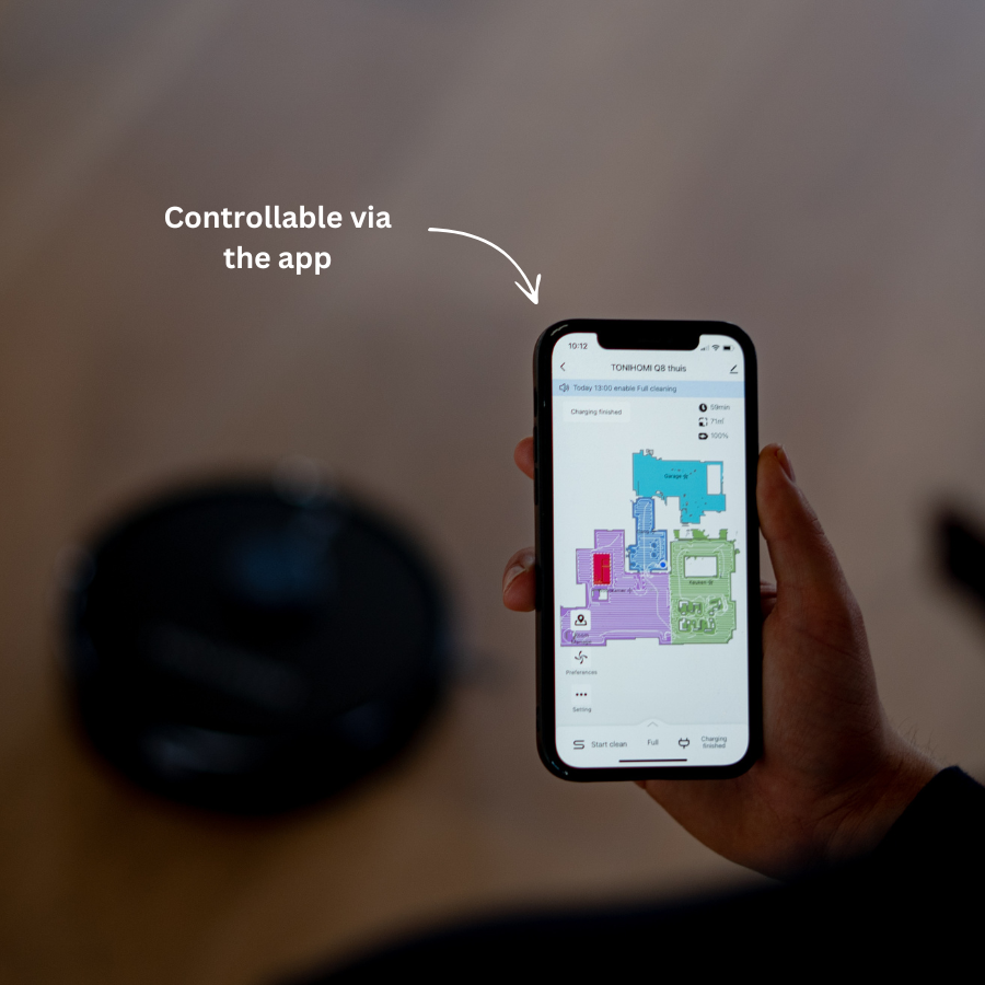 Eine Person hält ein Smartphone mit einer Roboterstaubsauger-App, der Staubsauger ist im Hintergrund verschwommen.