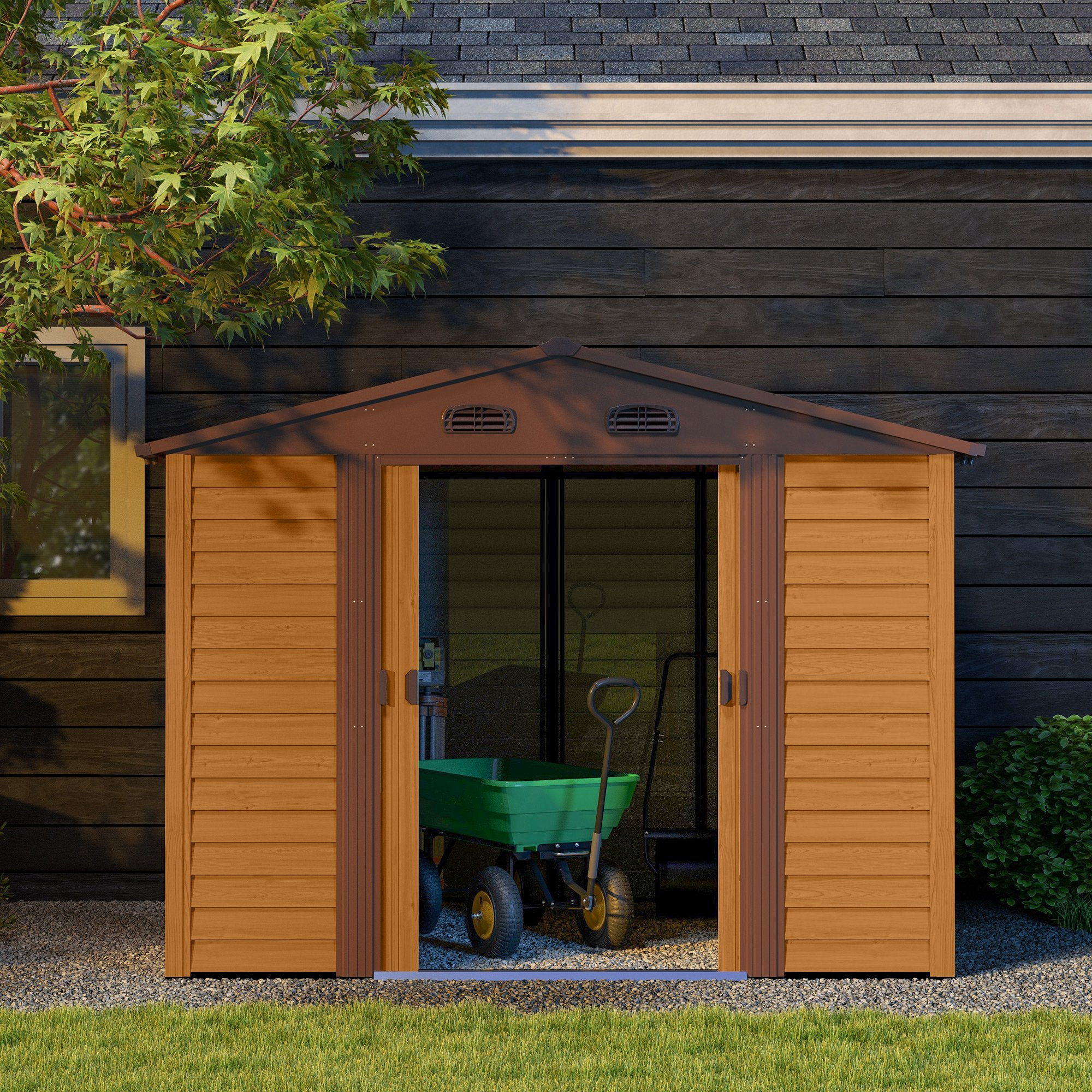 Un cobertizo de color madera con puerta abierta sobre grava, con un carrito de jardín verde dentro.