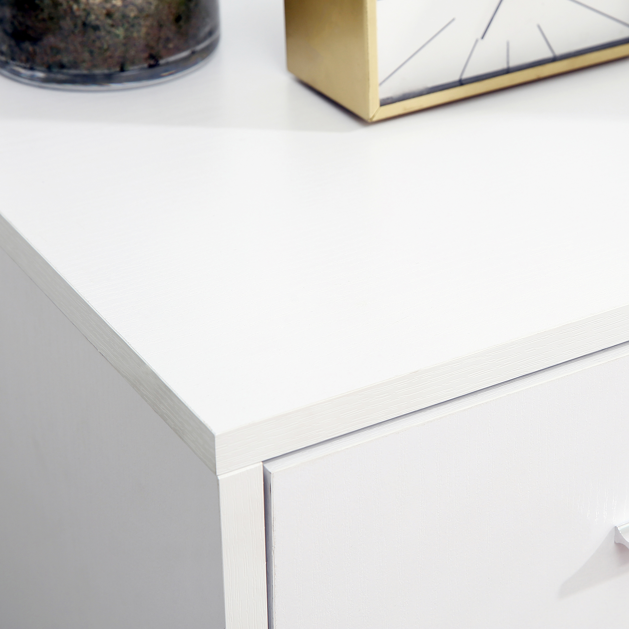 Una cómoda blanca con superficie lisa, un cajón y elementos decorativos encima.