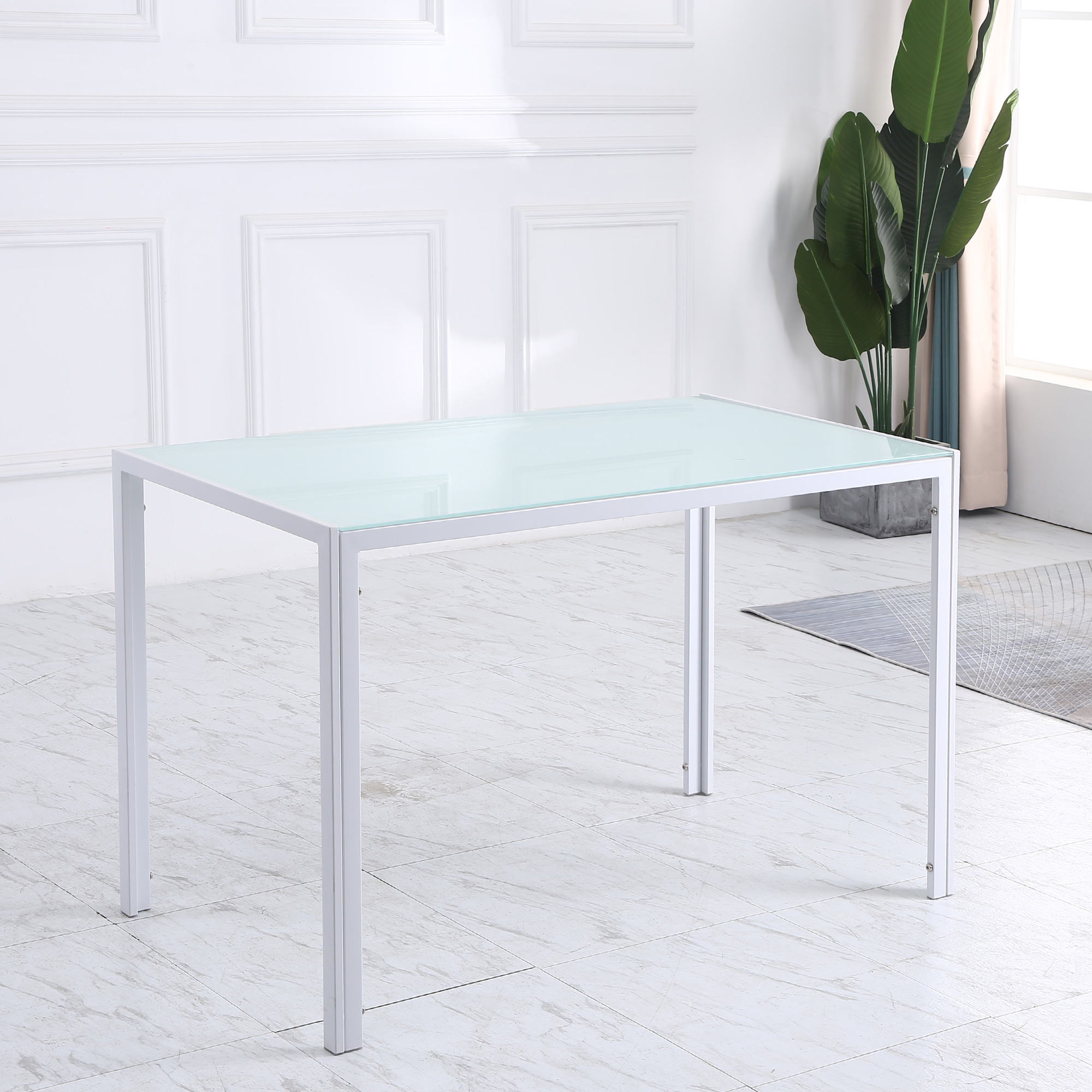 Una mesa blanca moderna con tapa de vidrio en una habitación luminosa con una planta en maceta y suelo de mármol.