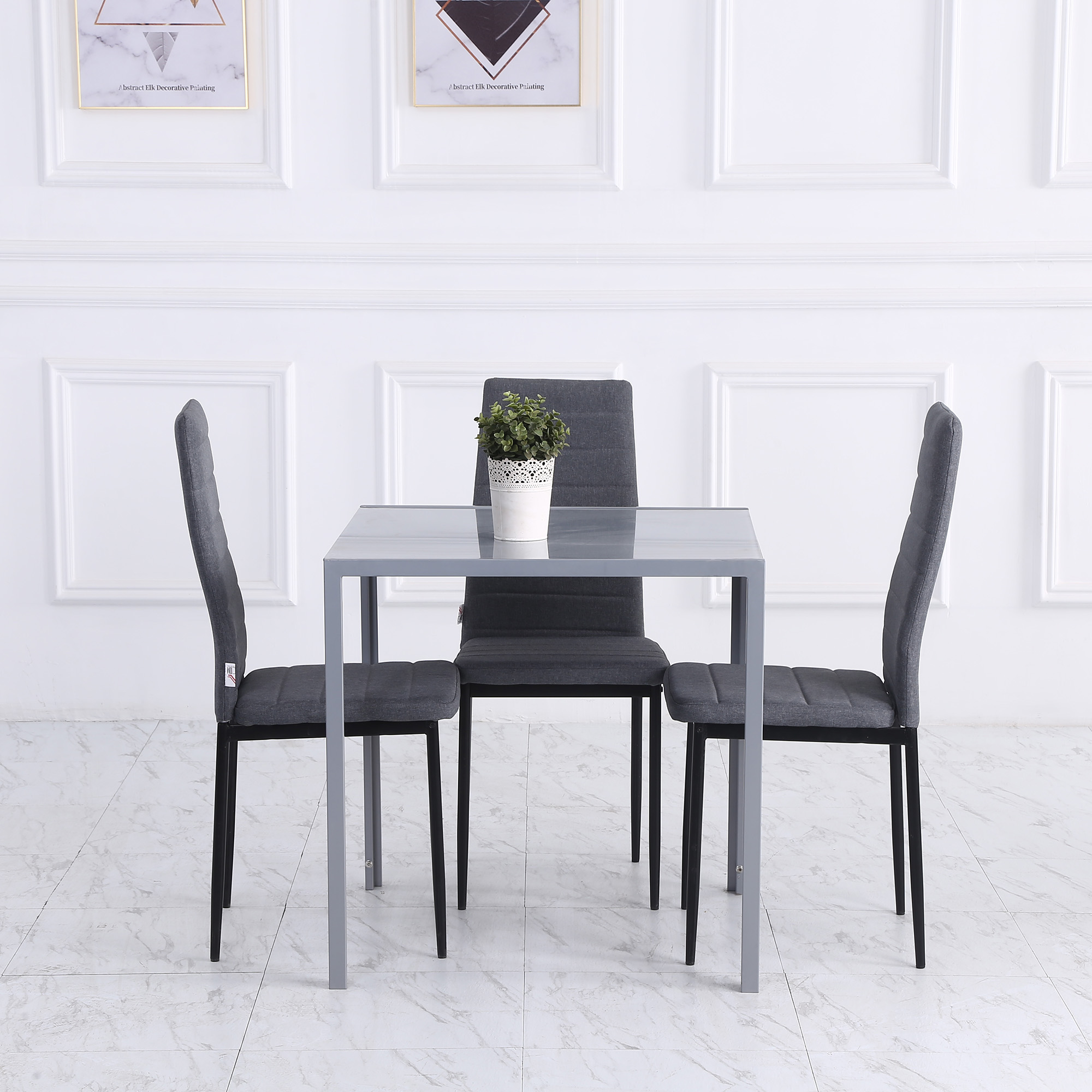 Una mesa de comedor gris con tres sillas a juego y una pequeña planta en maceta en una habitación blanca.