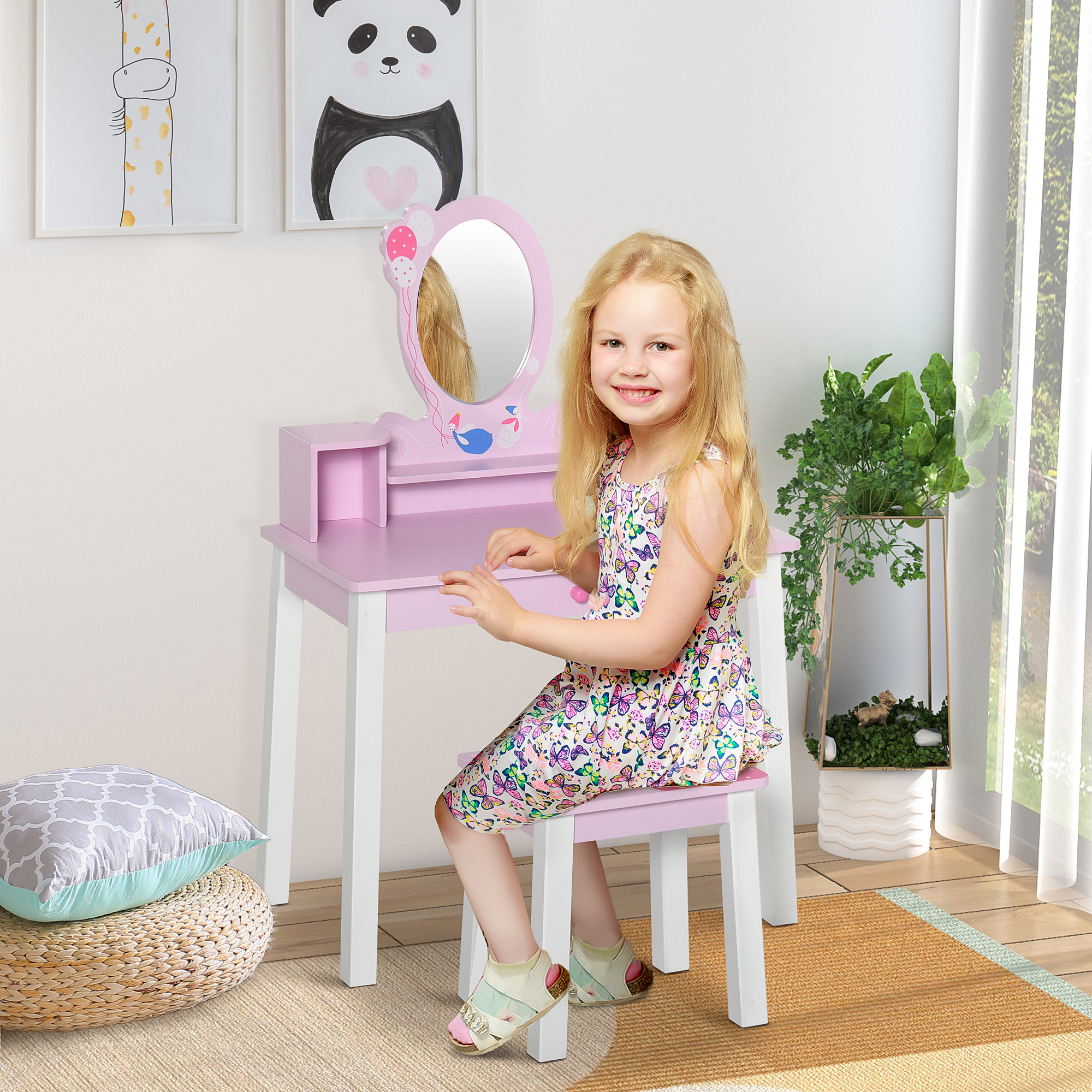 Una niña rubia con vestido de verano está sentada ante un tocador rosa y sonríe a la cámara.