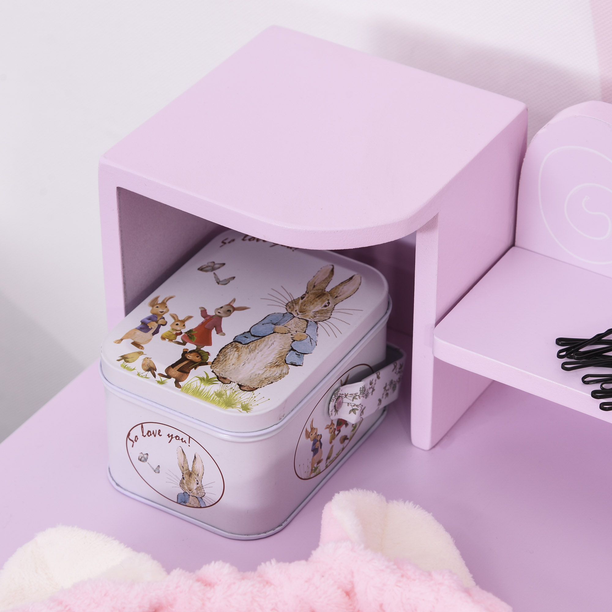 Una caja de hojalata blanca con ilustraciones de Perico el Conejo bajo una pequeña mesa rosa.