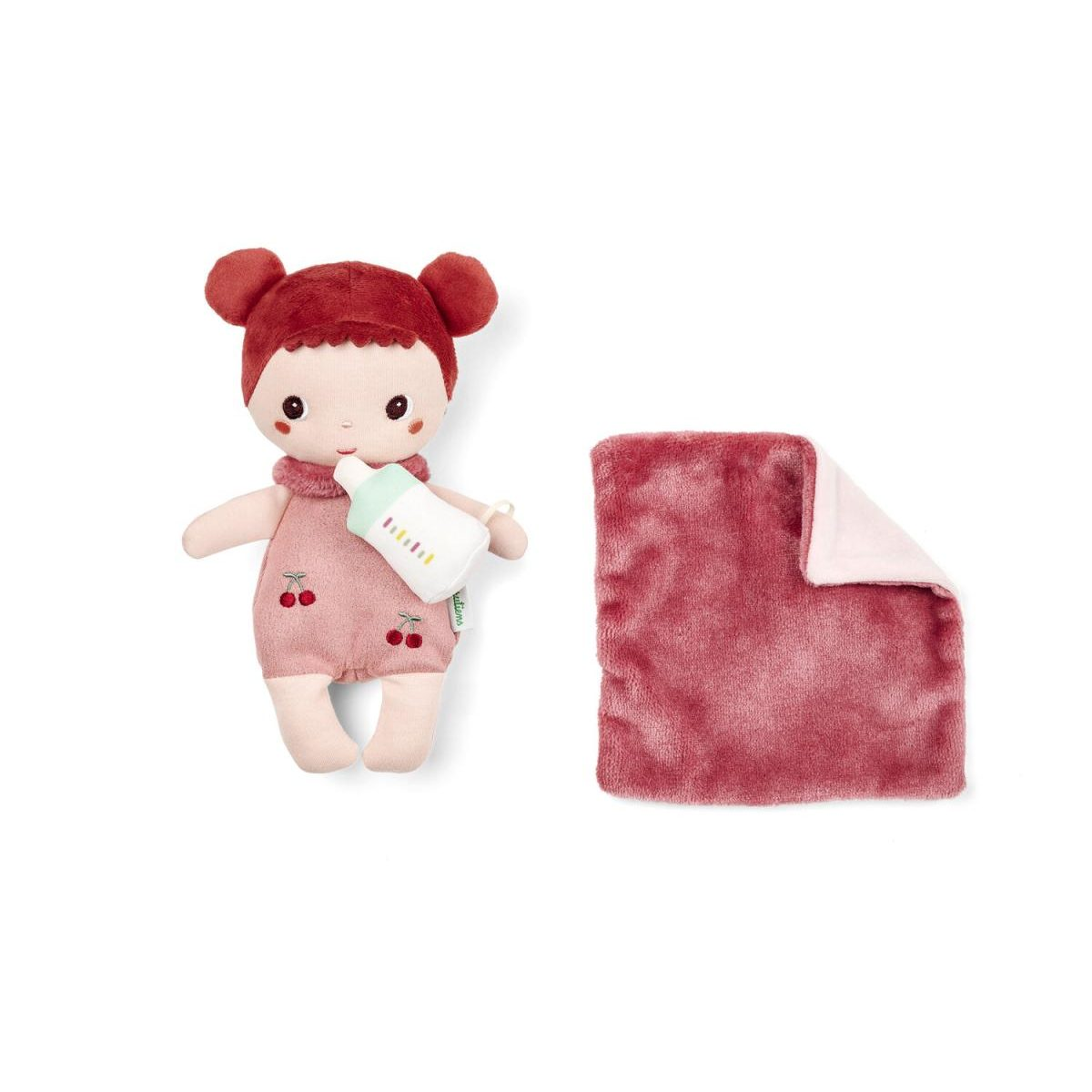 Eine Plüschpuppe mit roten Haaren und Kirsch-Latzhose hält eine Spielzeugflasche neben einer gefalteten rosa Decke.