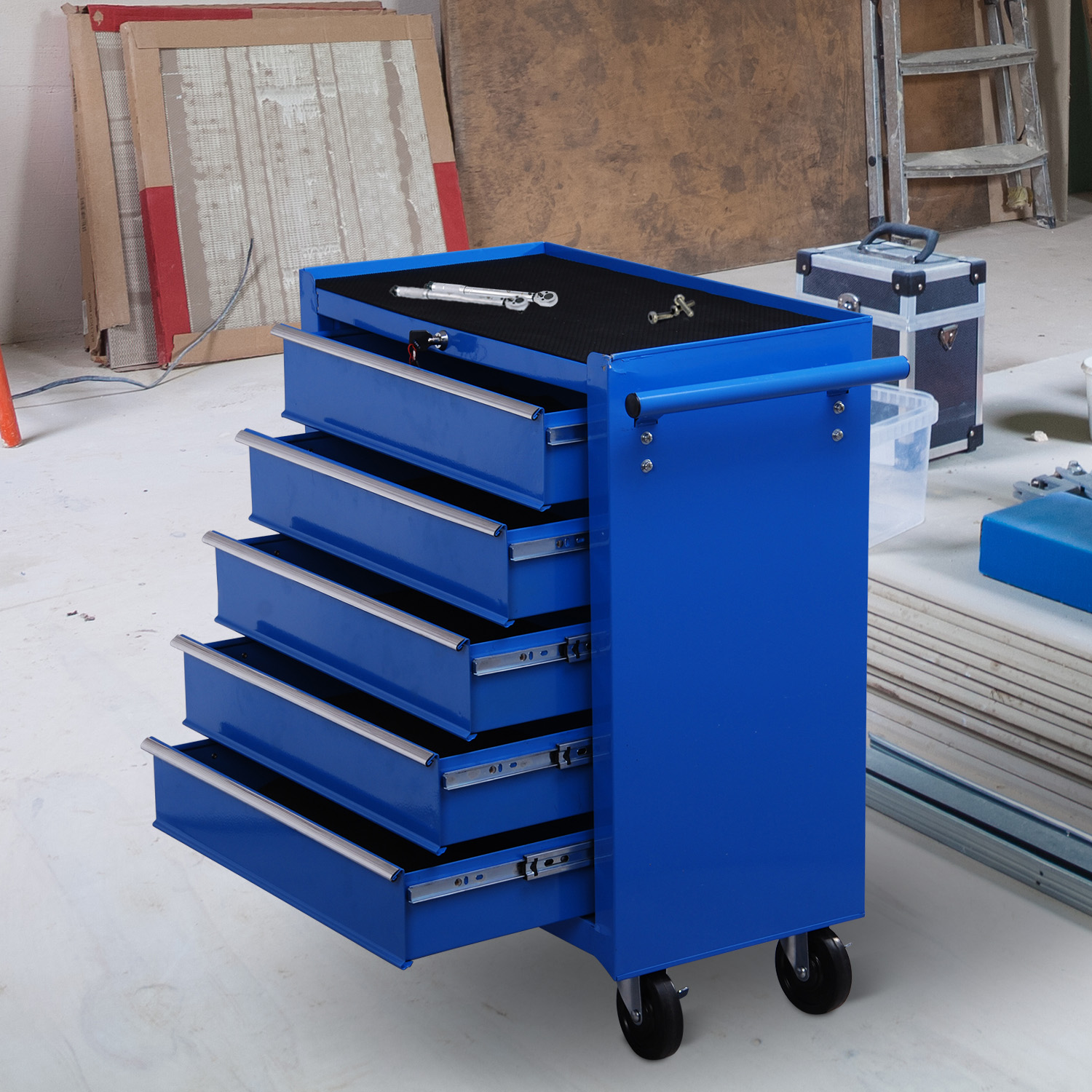Un carro de herramientas azul con cinco cajones abiertos se encuentra en un taller, rodeado de materiales de construcción.