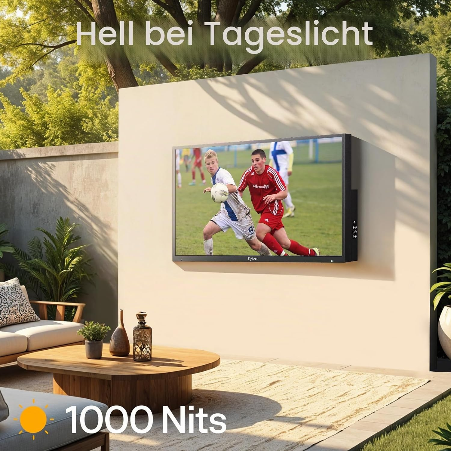Un televisor de exterior en una pared muestra un partido de fútbol en un patio soleado.