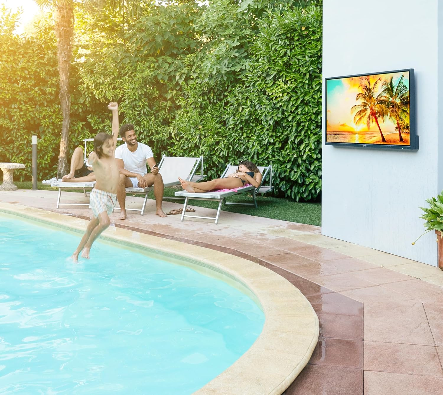 Un niño salta a una piscina mientras la familia se relaja en tumbonas y hay una TV en la pared.