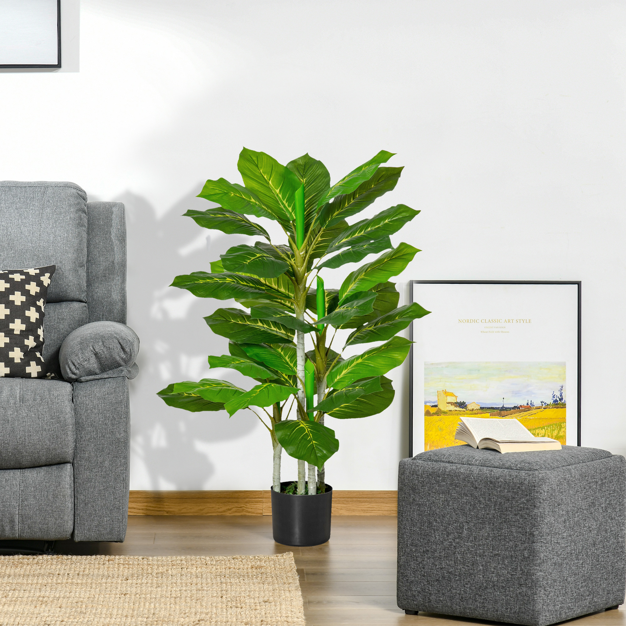 Una planta artificial verde en maceta se encuentra junto a un sillón gris y un taburete gris a juego con un libro abierto.