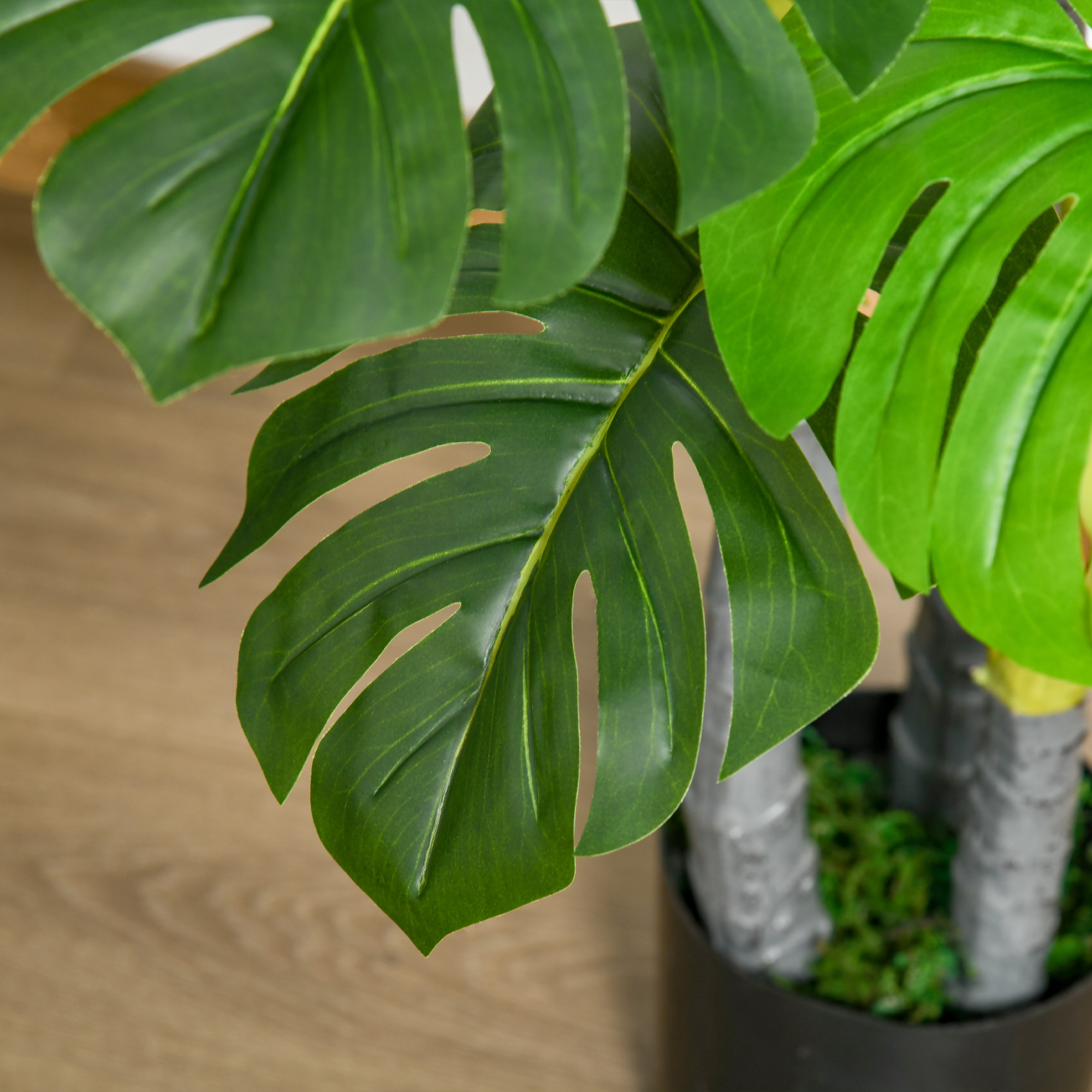 Primer plano de grandes hojas verdes de una planta artificial de monstera en una maceta oscura.