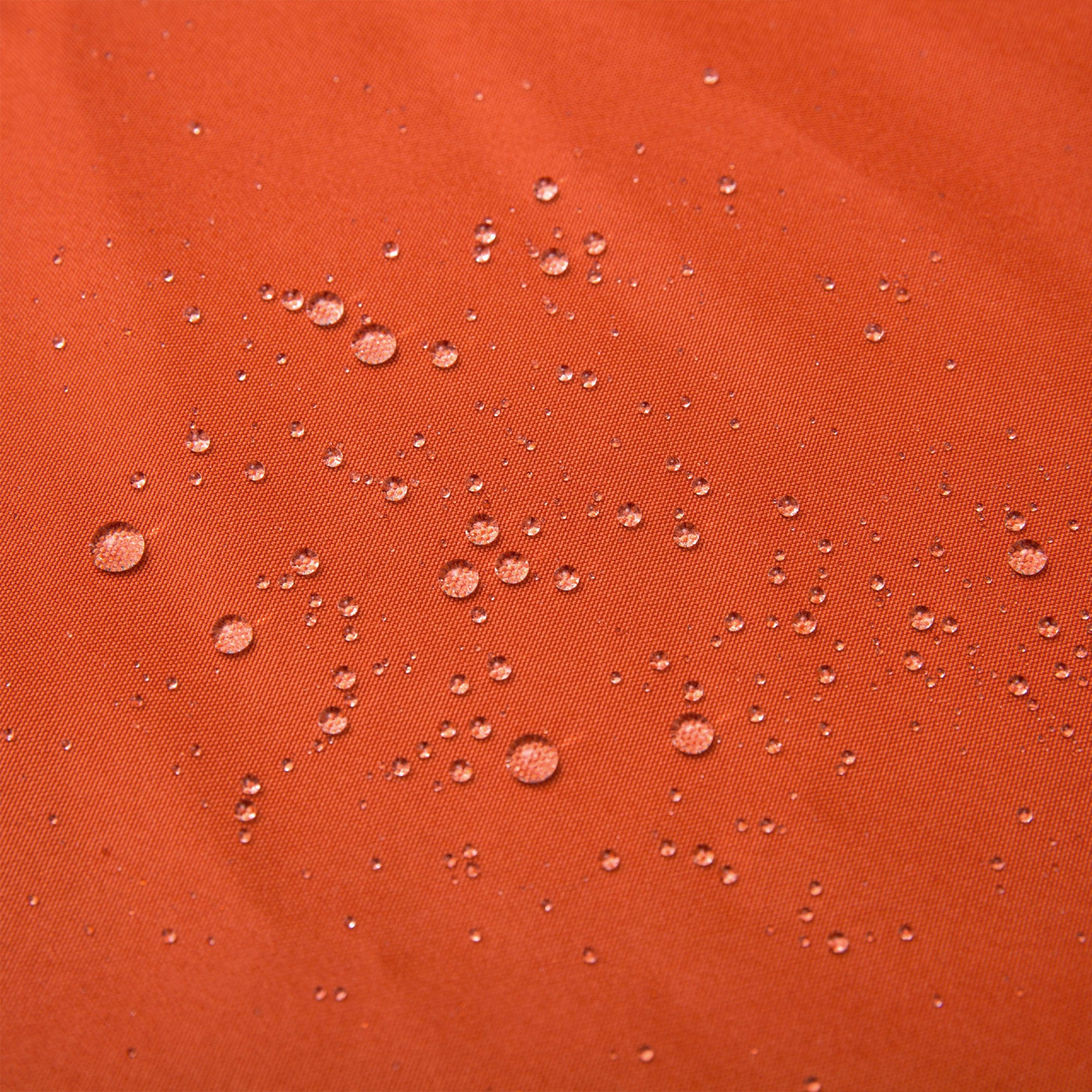 Las gotas de agua se acumulan en un tejido impermeable de color naranja brillante y texturizado.