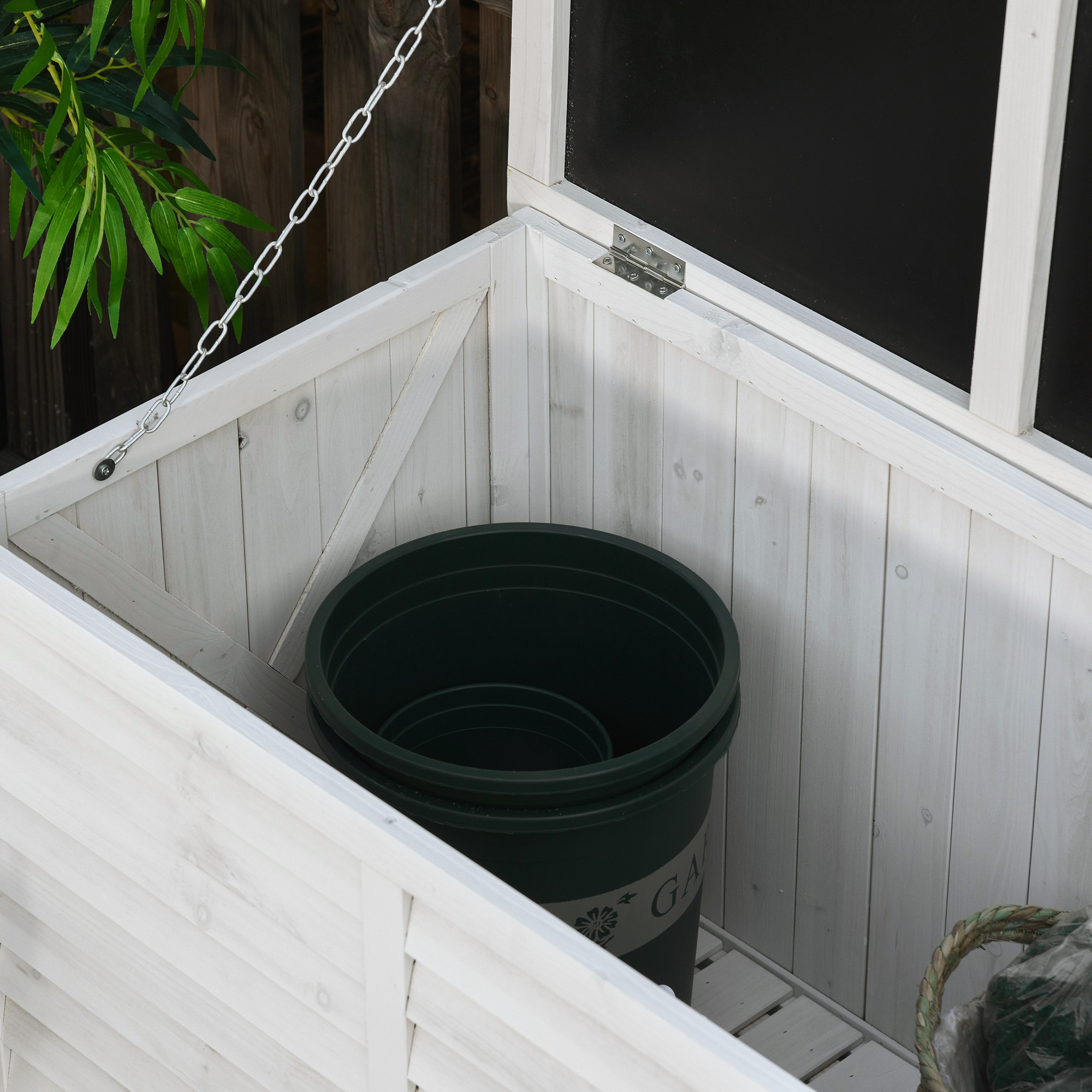 Una caja de madera blanca abierta con macetas verdes dentro, sobre una terraza de madera.