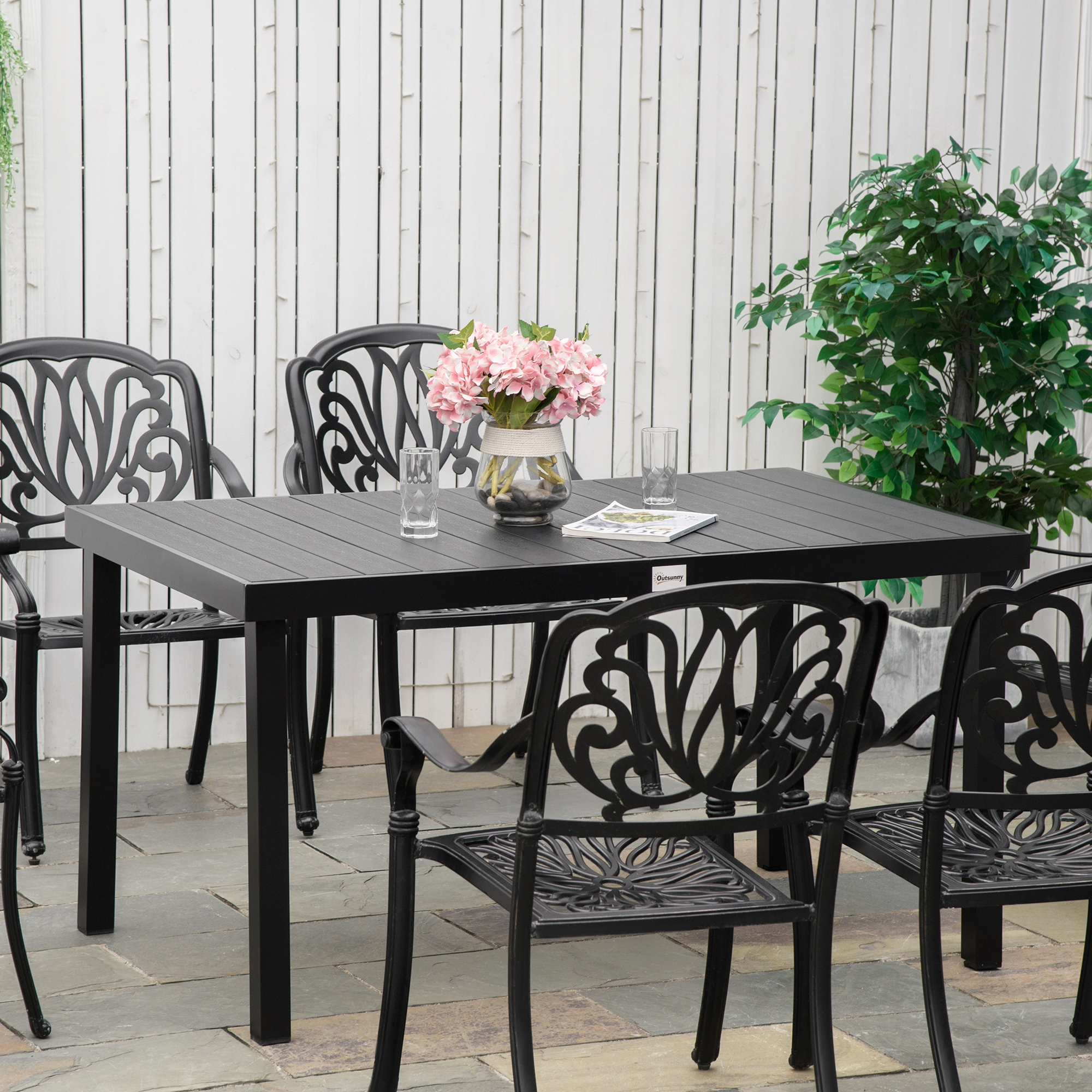 Una mesa negra con cuatro sillas y flores rosadas en un jarrón en un patio.
