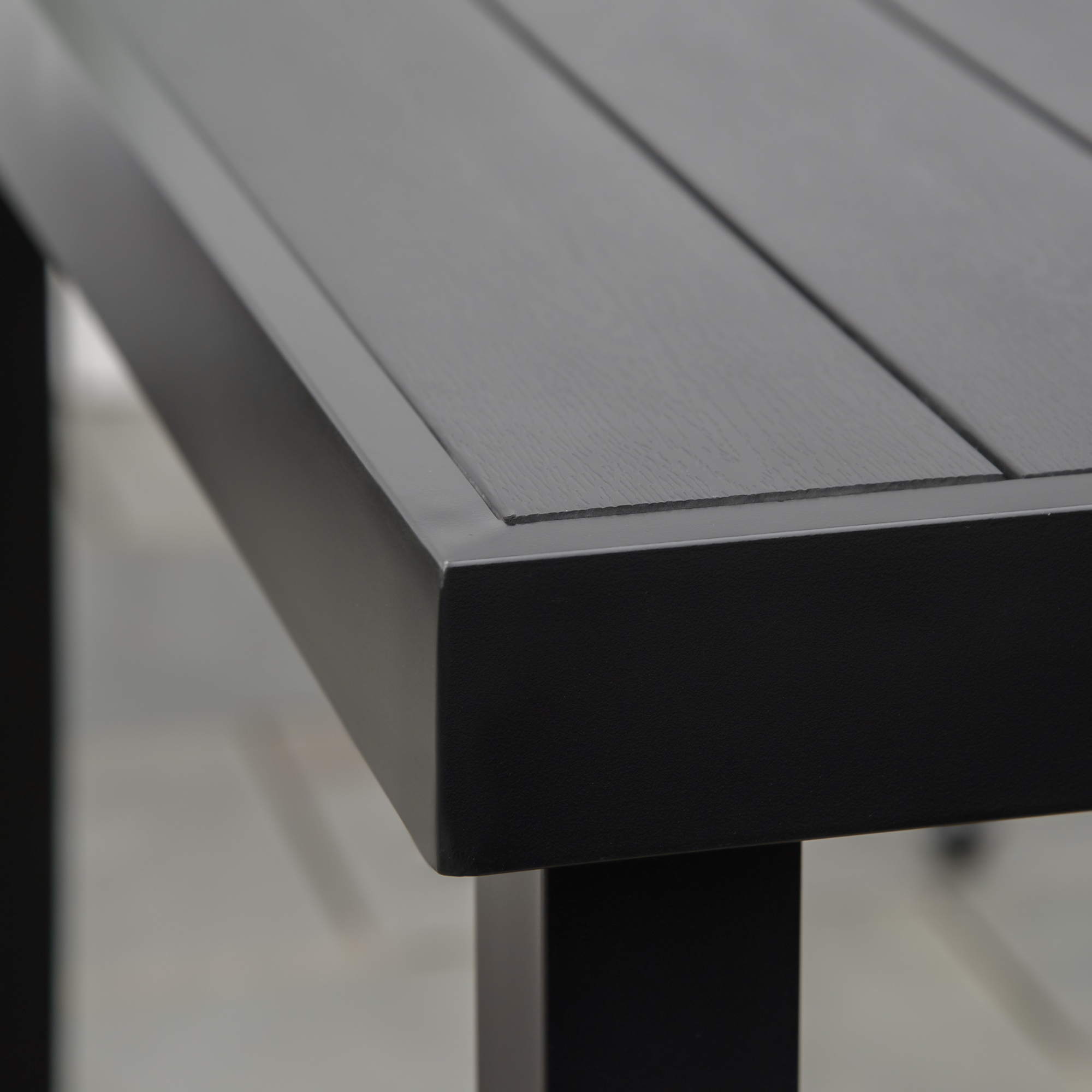 Primer plano de la esquina de una mesa negra moderna con tablero de listones y marco metálico sobre suelo gris.
