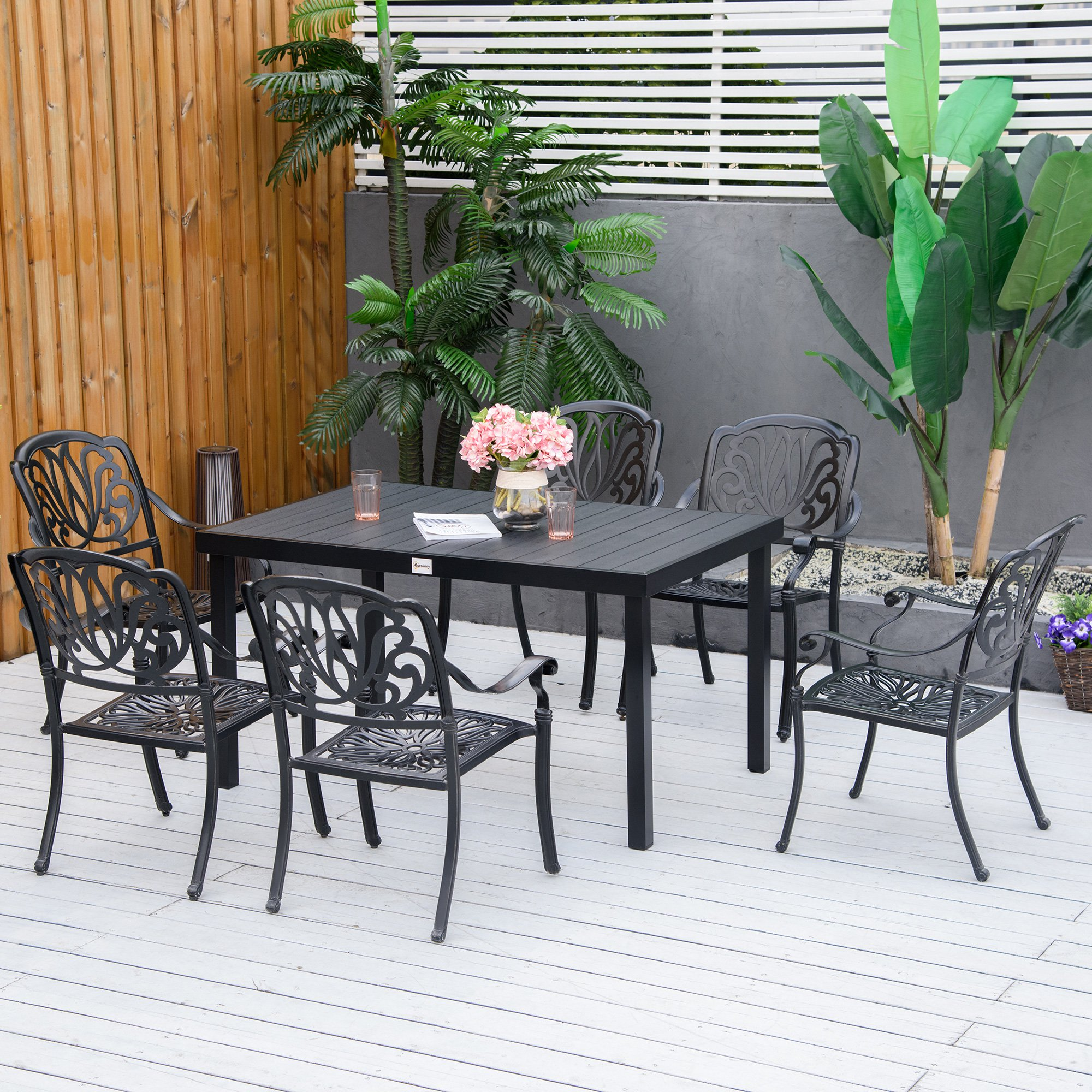 Un juego de comedor de metal negro para patio con seis sillas y una mesa con flores en una cubierta de madera blanca.