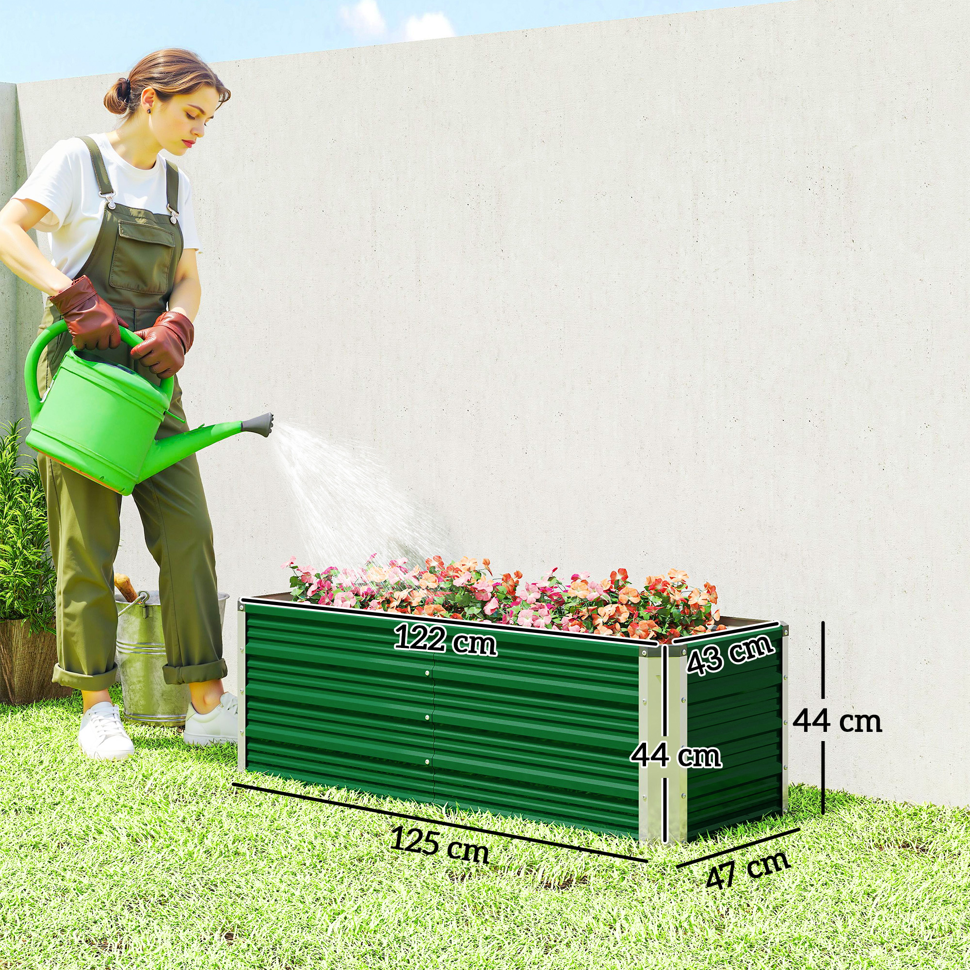 Una mujer con peto verde riega un arriate verde y largo con flores rojas, mostrando las dimensiones.