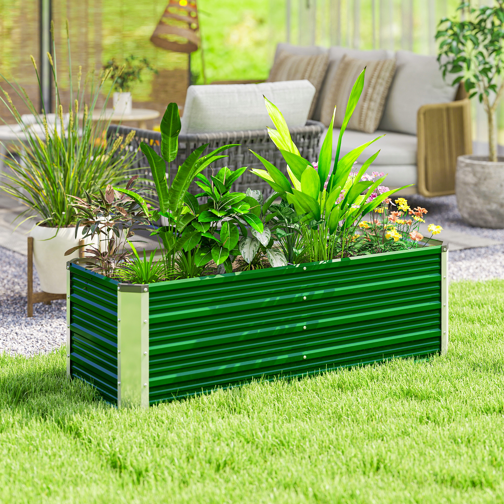 Un arriate elevado de metal verde con varias plantas sobre el césped, con una terraza al fondo.