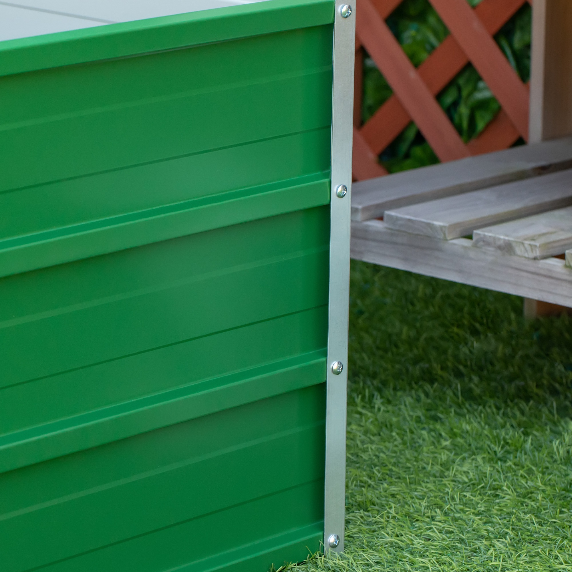 Cama de metal verde con ribete plateado sobre césped artificial.