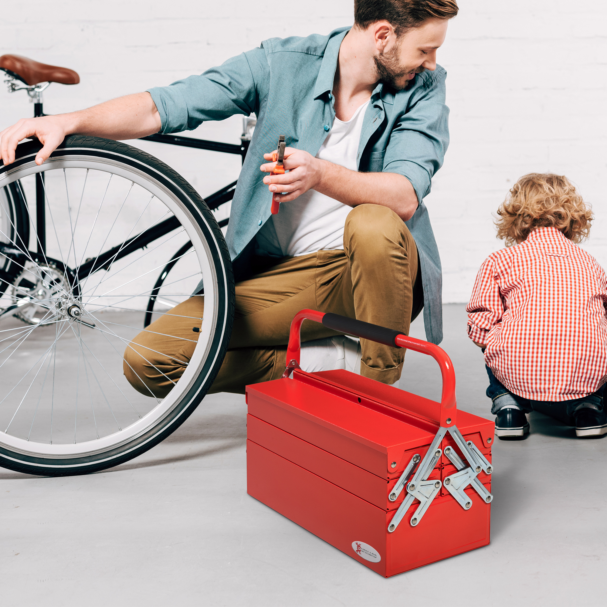 Un hombre repara una bicicleta cerca de una caja de herramientas roja mientras un niño observa.