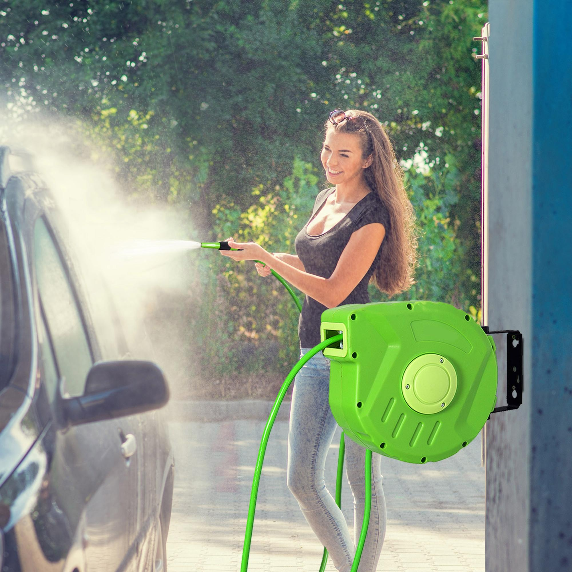 Una mujer lava un coche usando una manguera verde conectada a un carrete de pared.