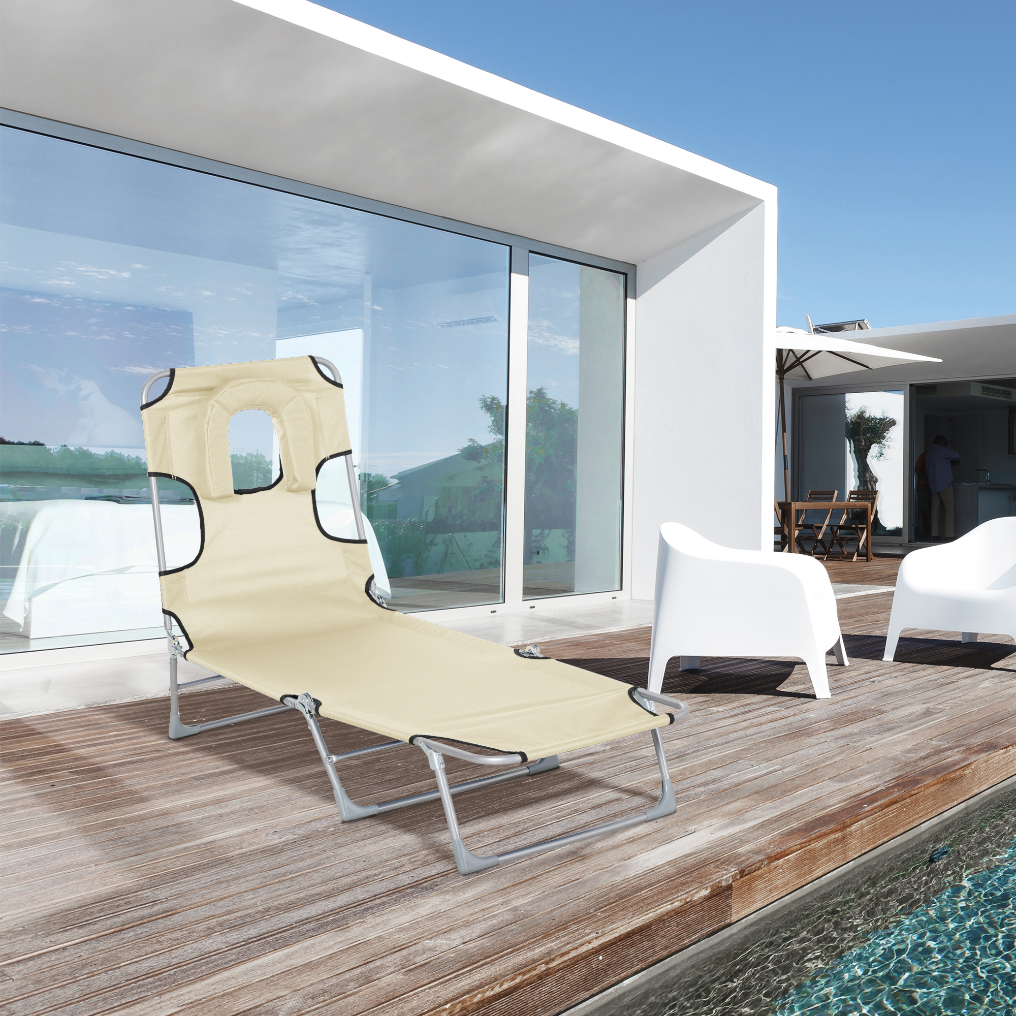 Una tumbona beige junto a la piscina de una villa blanca moderna bajo el cielo azul.