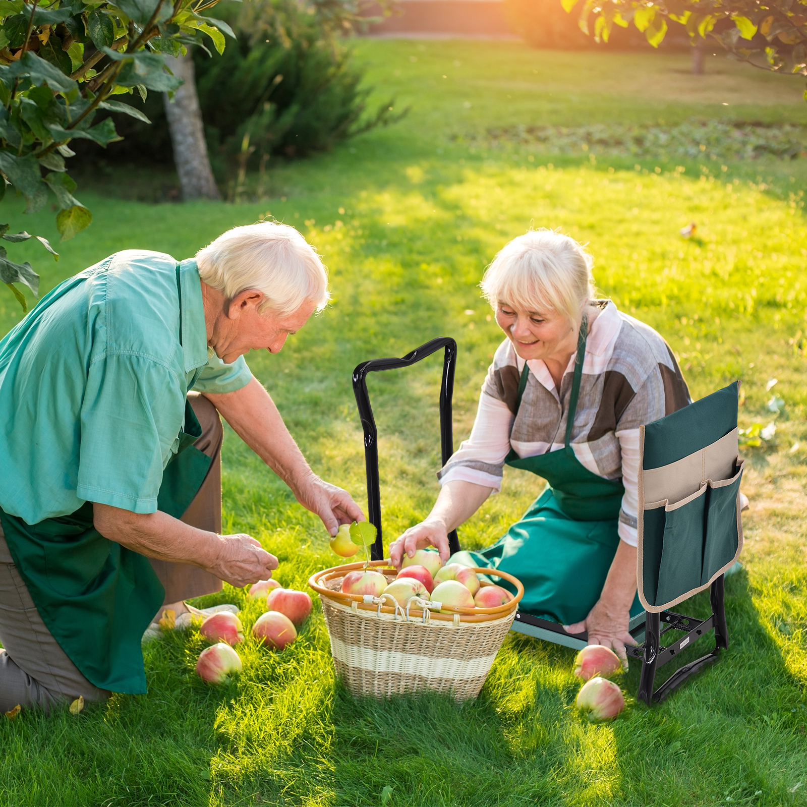 Pareja mayor en un jardín arrodillada junto a una cesta de mimbre llena de manzanas.
