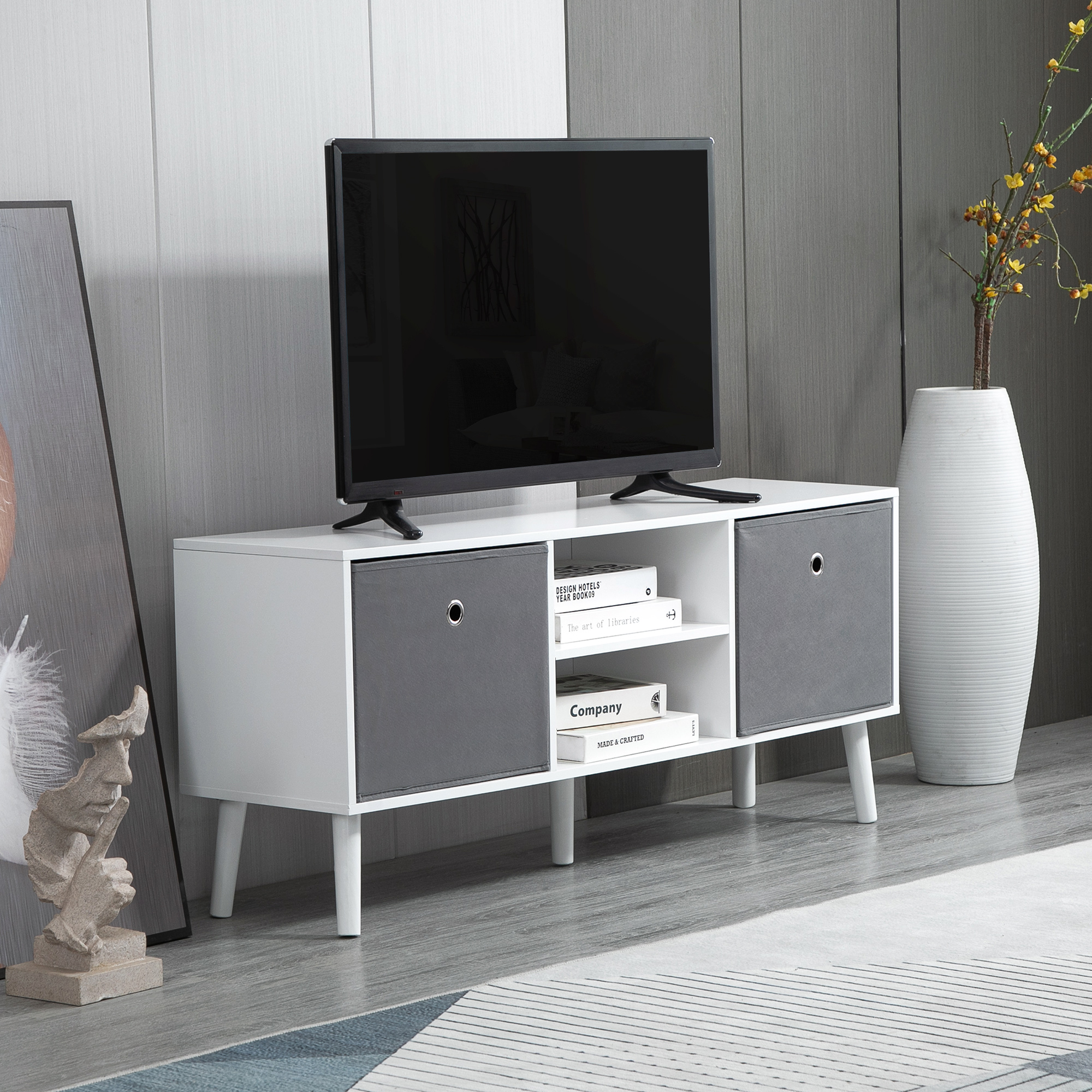 Un mueble de TV blanco con cajones de tela gris, libros y un televisor está ubicado en una habitación moderna.