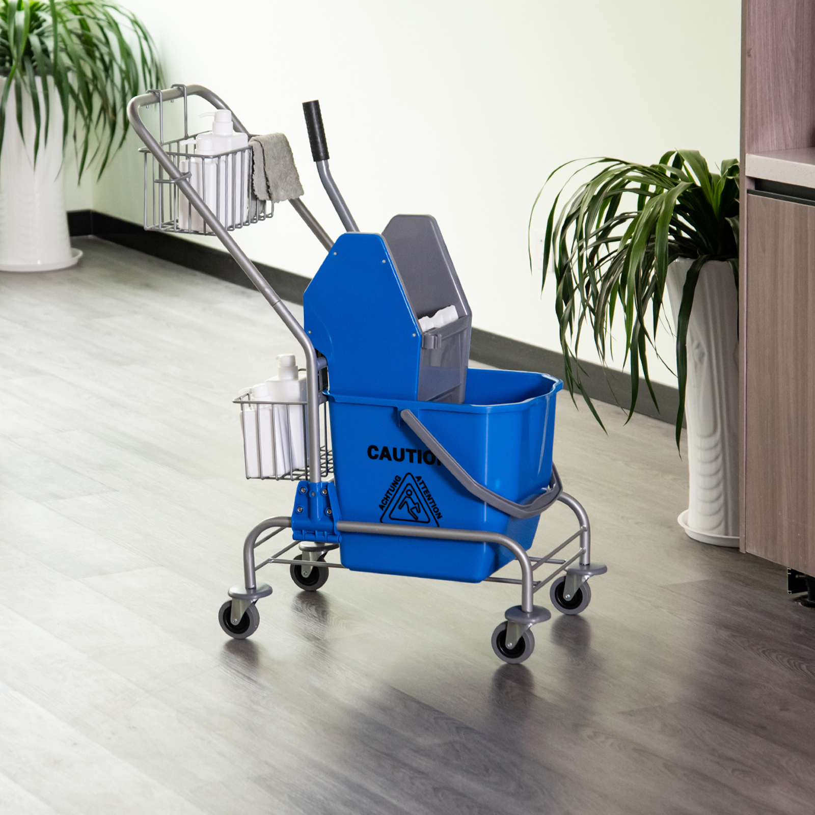 Un carrito de limpieza azul con cubo, escurridor y suministros sobre suelo de madera.