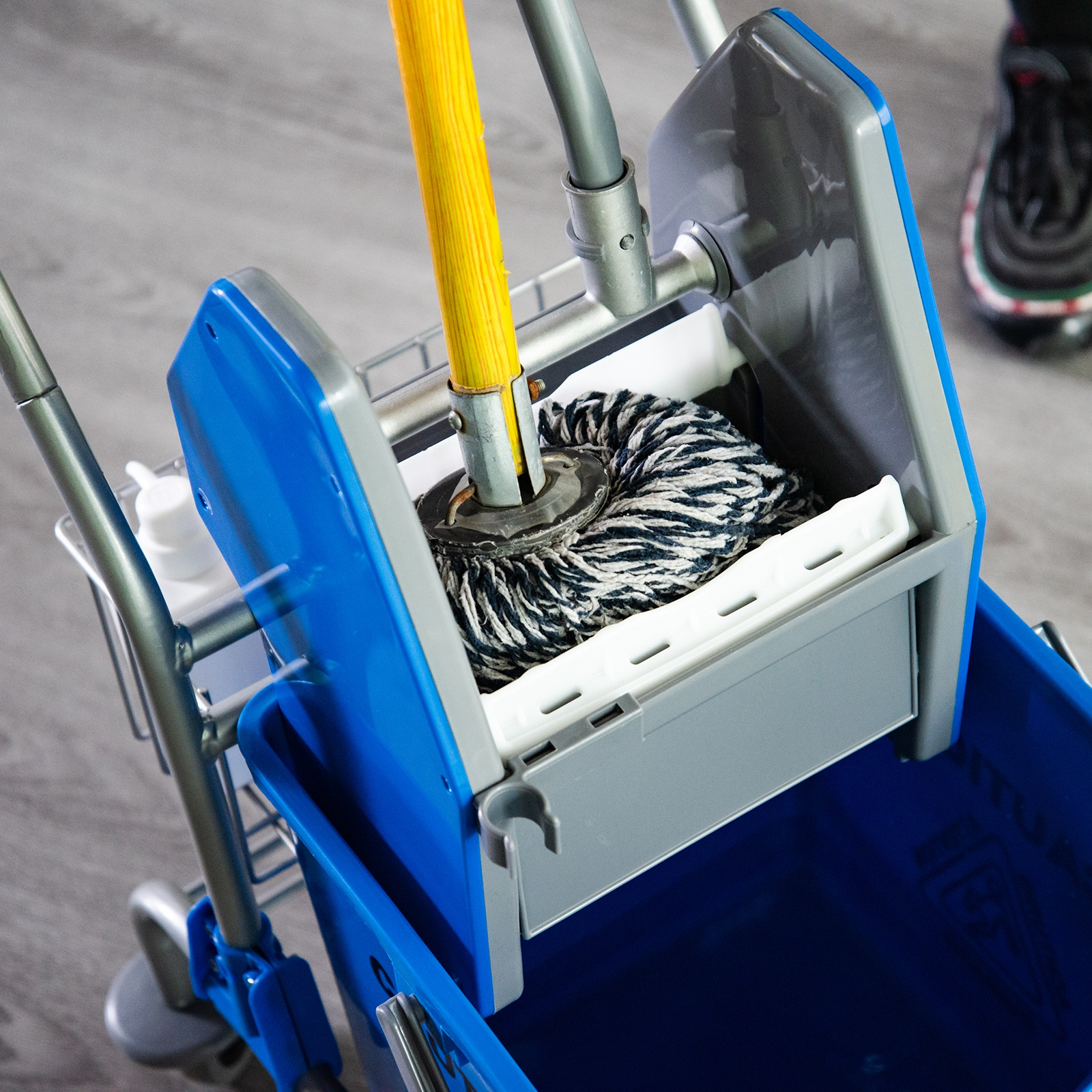 Un carrito de limpieza azul con una fregona en un cubo sobre suelo gris.