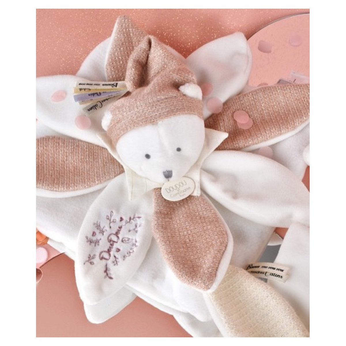 Ein weiß-goldener Kuscheltier-Teddybär auf einer rosafarbenen, glitzernden Decke mit Konfetti.