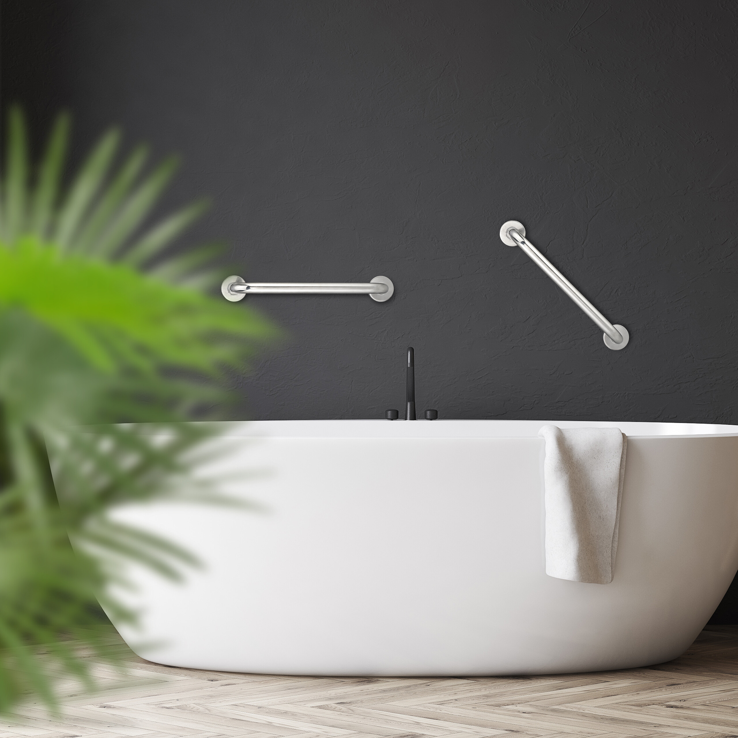 Eine weiße Badewanne vor einer dunklen Wand mit Haltegriffen und einem Handtuch. Im Vordergrund grüne Pflanzen.