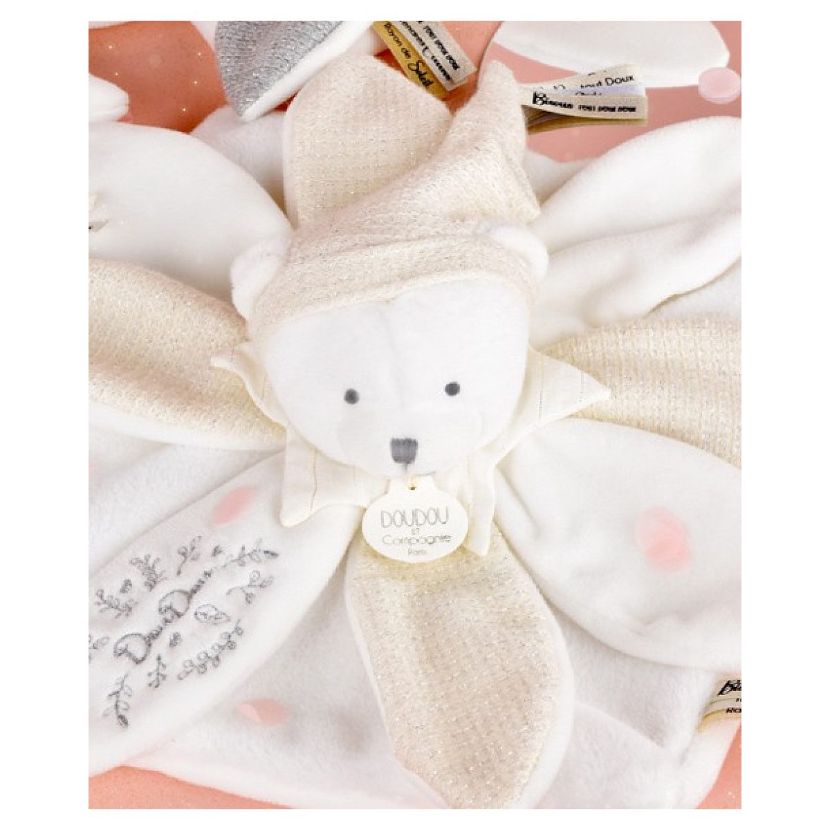Eine weiße Kuscheldecke mit Plüschbär, glitzernden Goldakzenten, Doudou-Etikett und Blumenstickerei.