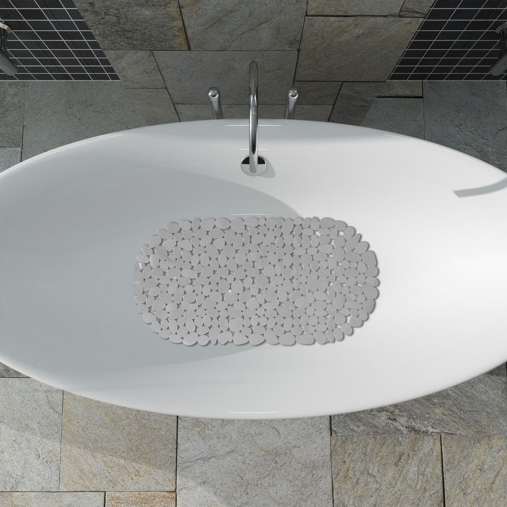 Eine ovale weiße Badewanne mit grauer Steinbadematte von oben vor Steinfliesen.