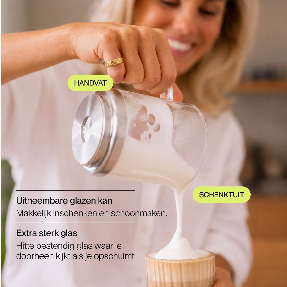 Une femme verse du lait moussu d'un pichet en verre avec un couvercle en inox dans une tasse.