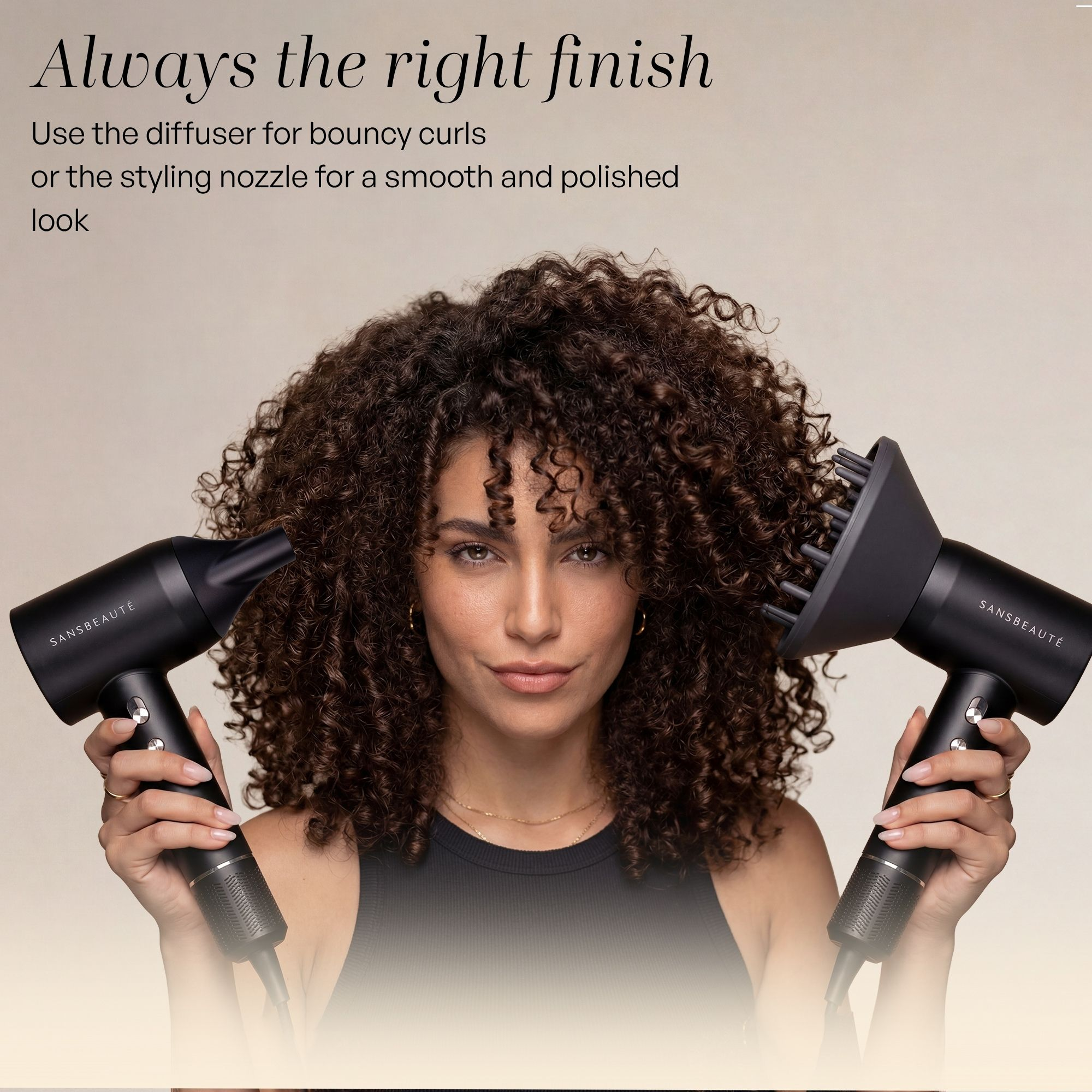 Una donna con i capelli ricci tiene un asciugacapelli nero con diversi accessori in ogni mano.