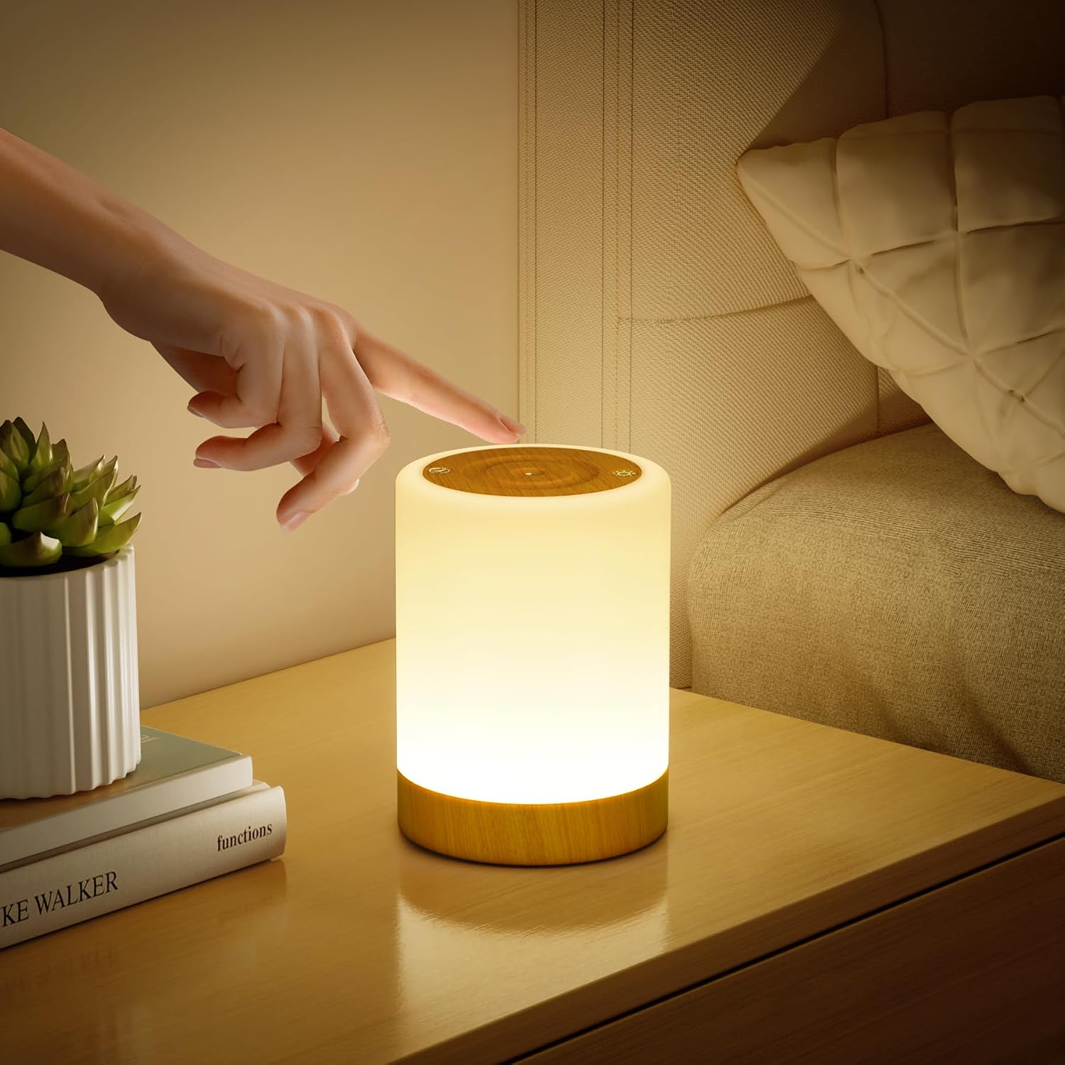 Eine Hand berührt eine kleine, zylindrische Tischlampe auf einem Nachttisch neben einem Bett.