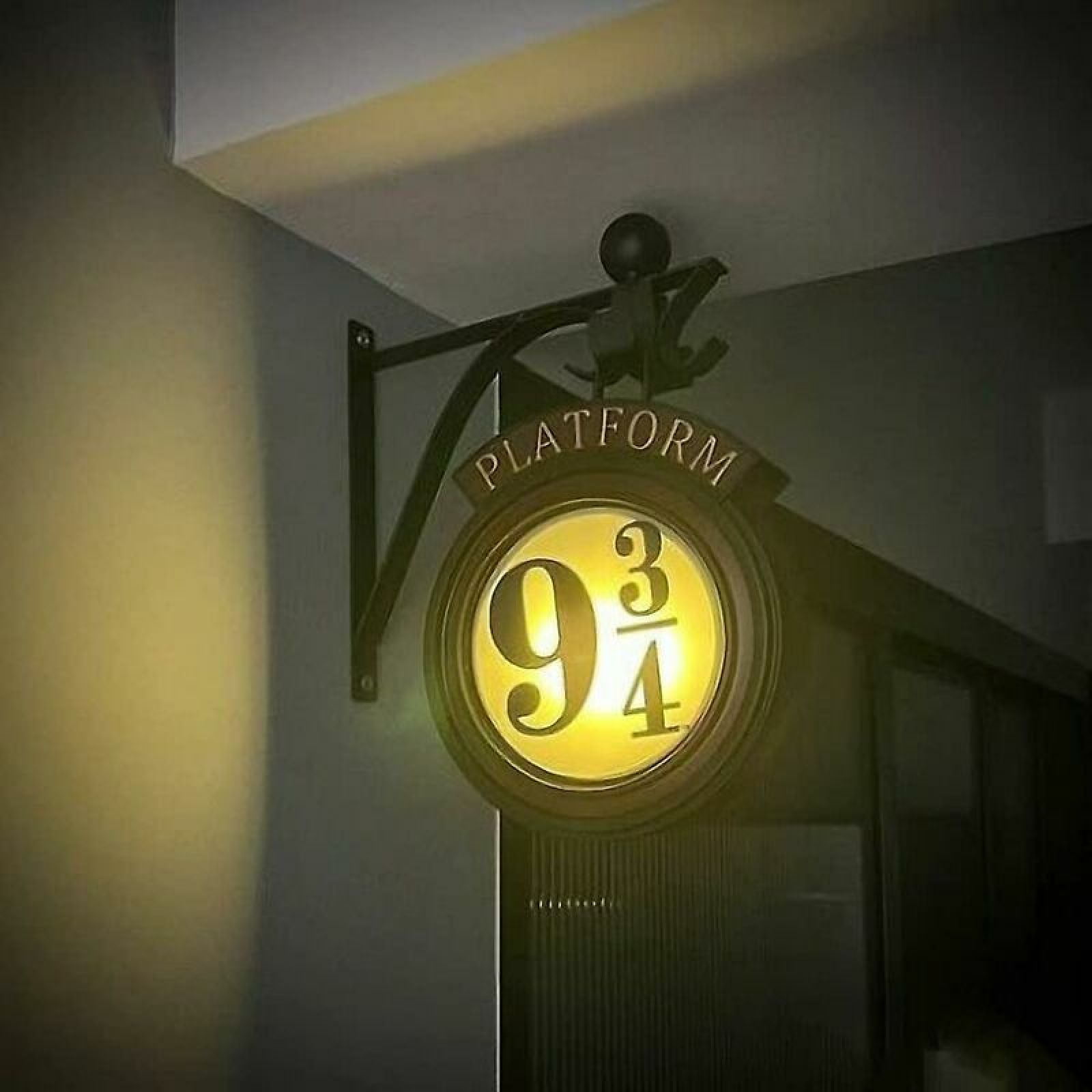Ein leuchtendes rundes Schild für Gleis 9 3/4 hängt an einer dunklen Metallhalterung.