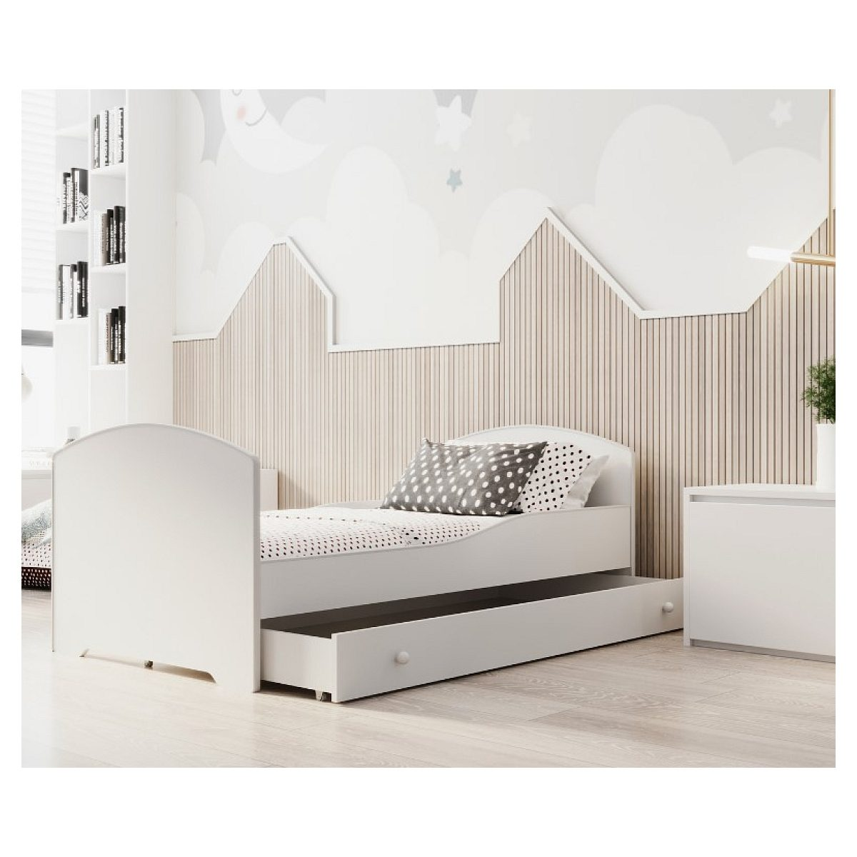 Ein weißes Kinderbett mit einer Ausziehhublade steht in einem Zimmer mit Holzwand und Wolkentapete.