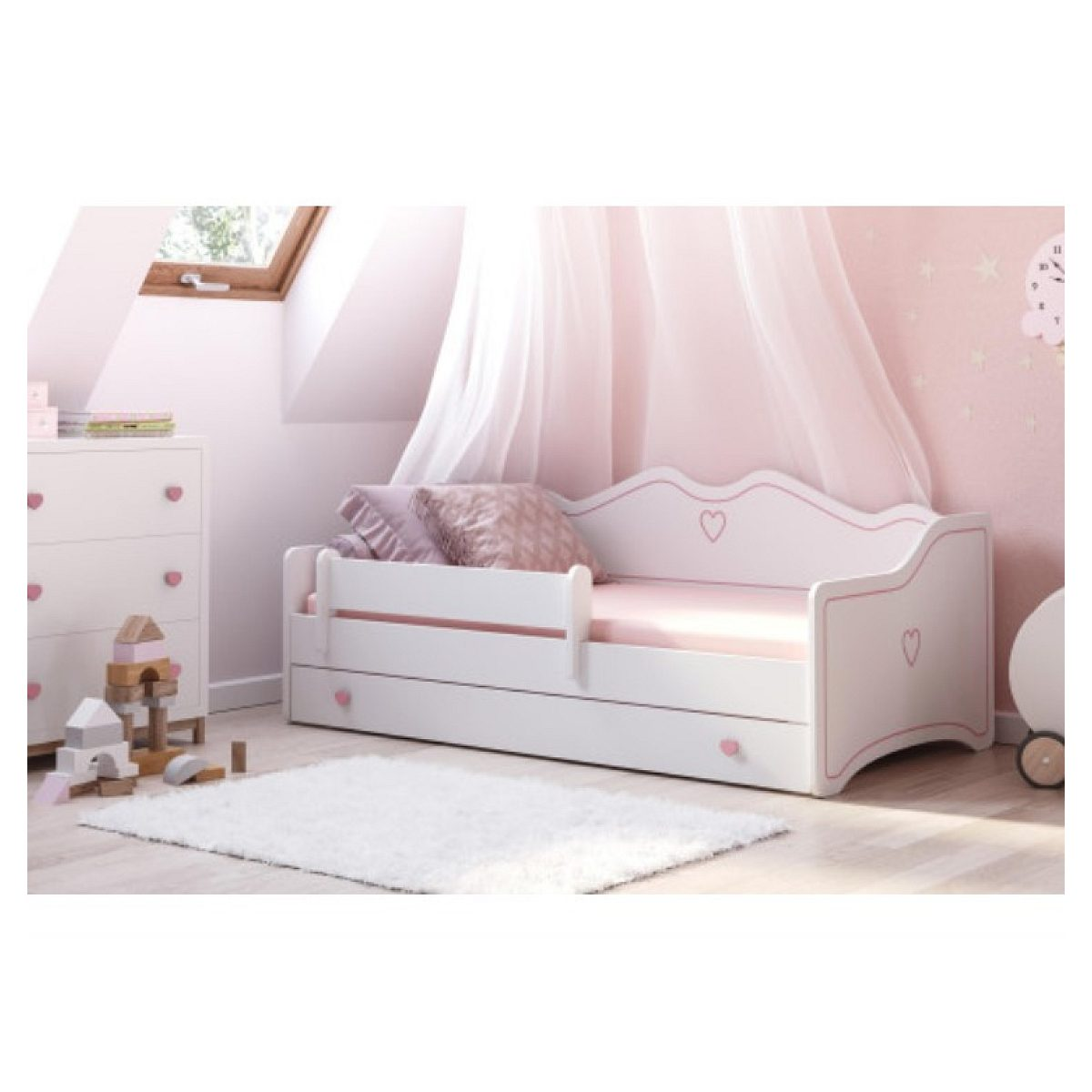 Ein weißes Kinderbett mit pinken Akzenten, Herzmotiven und einer Kuscheldecke in einem hellen Kinderzimmer.