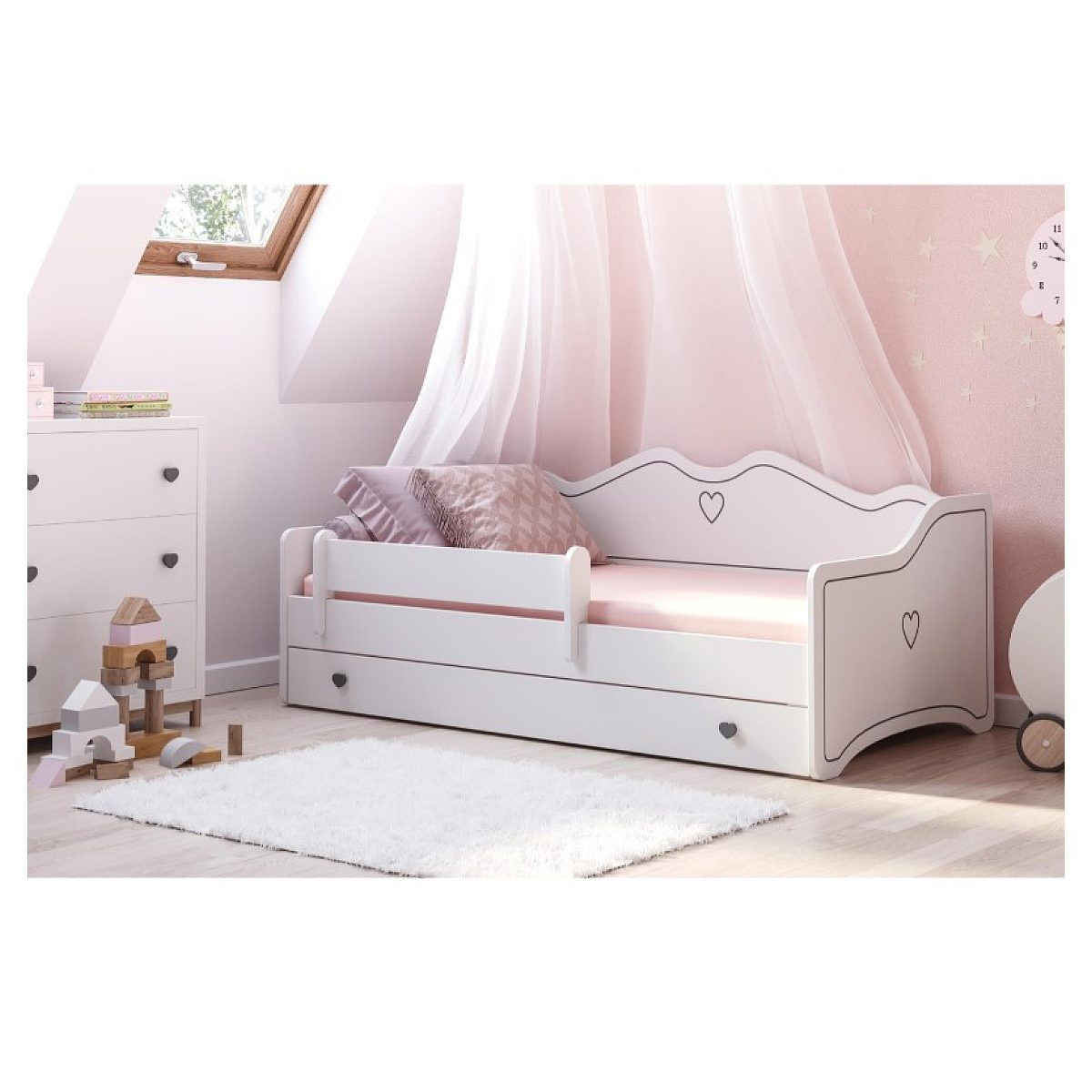 Ein weißes Kinderbett mit Herzmotiven in einem rosa Zimmer mit weißem Teppich, Kommode und Holzspielzeug.