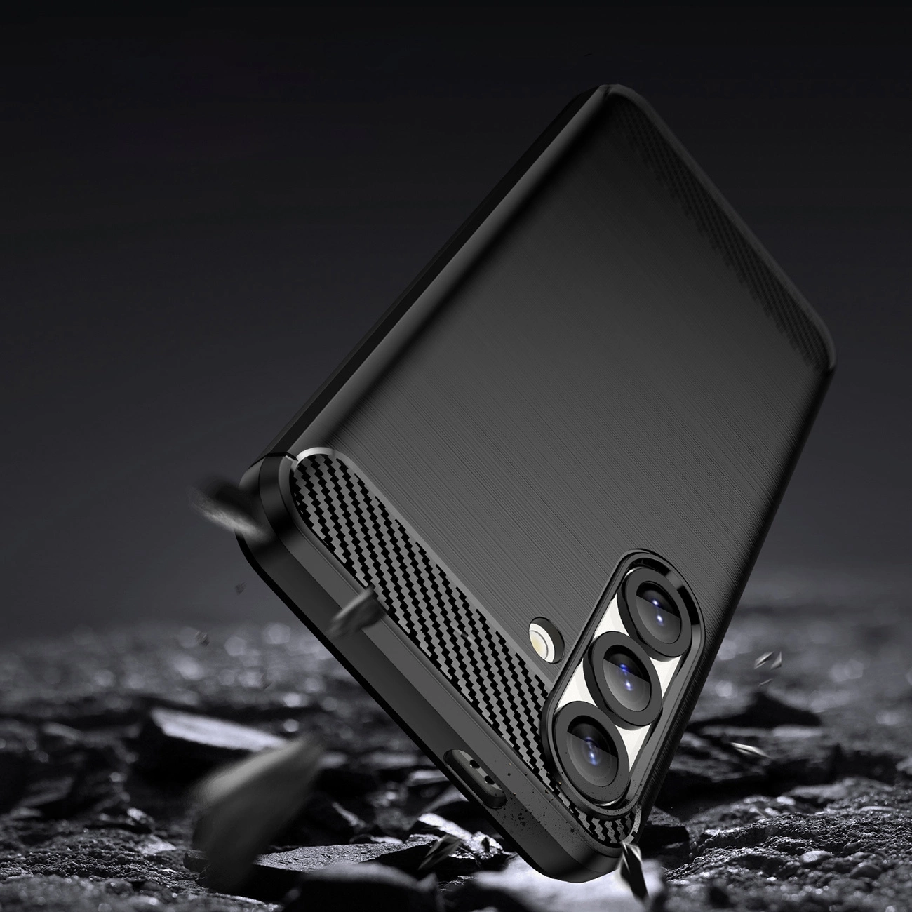 Uno smartphone nero con cover in fibra di carbonio su terreno fangoso e sfondo scuro.