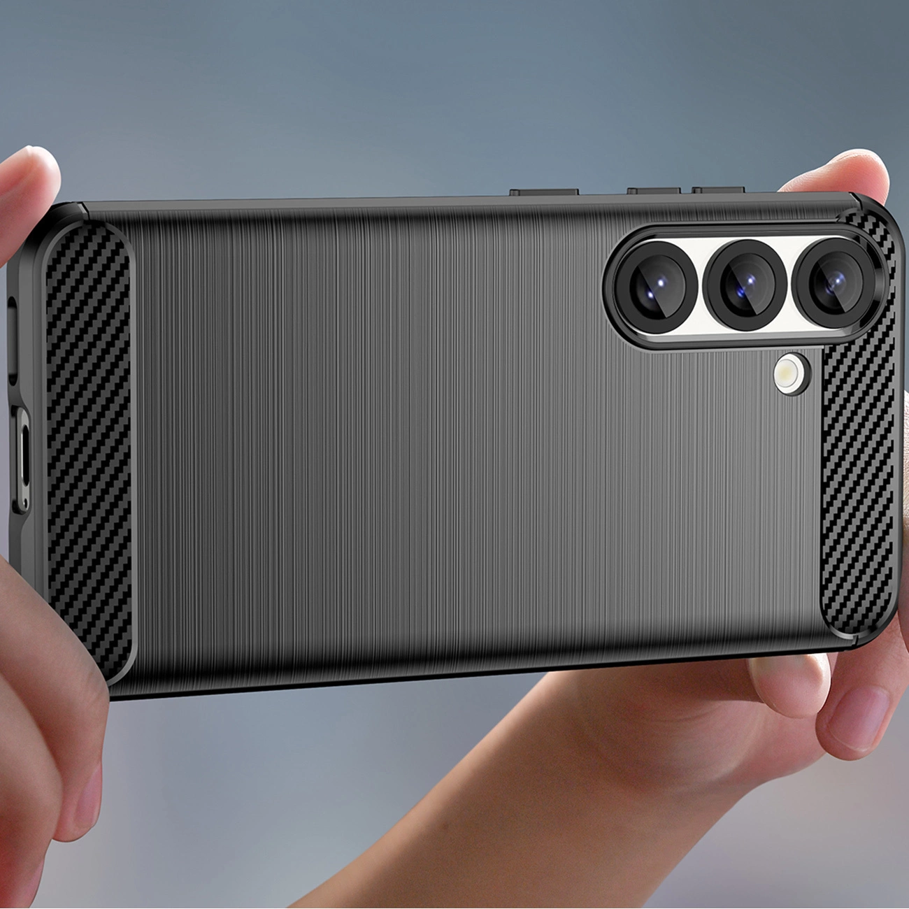 Uno smartphone viene tenuto in una custodia protettiva nera con design in metallo spazzolato e tre fotocamere.