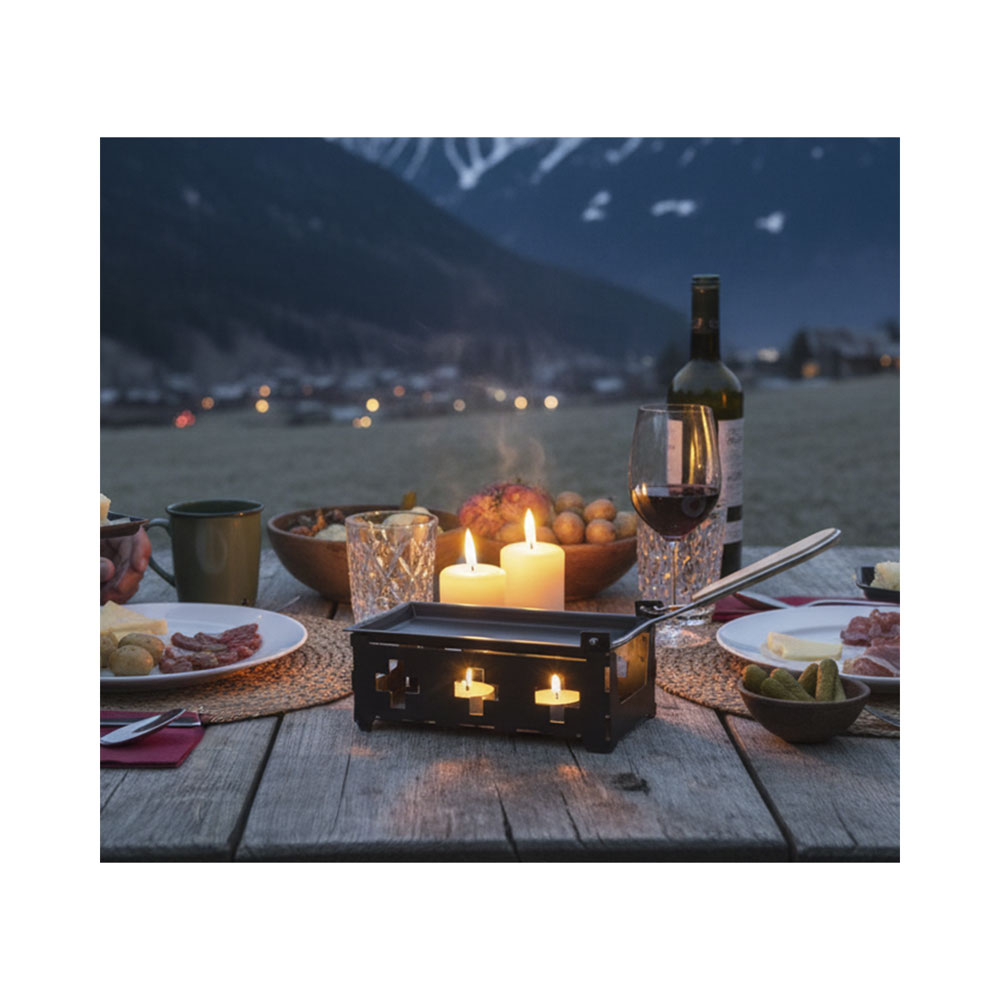 Raclette-Set mit Kerzen auf einem Holztisch im Freien, im Hintergrund schneebedeckte Berge.